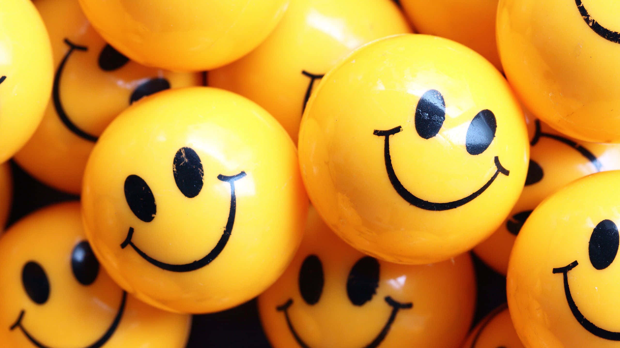 Smile Emoji 桌布 壁紙 — 一個特寫，顯示一堆帶有簡單黑色笑臉的光澤黃色球體堆疊在一起。