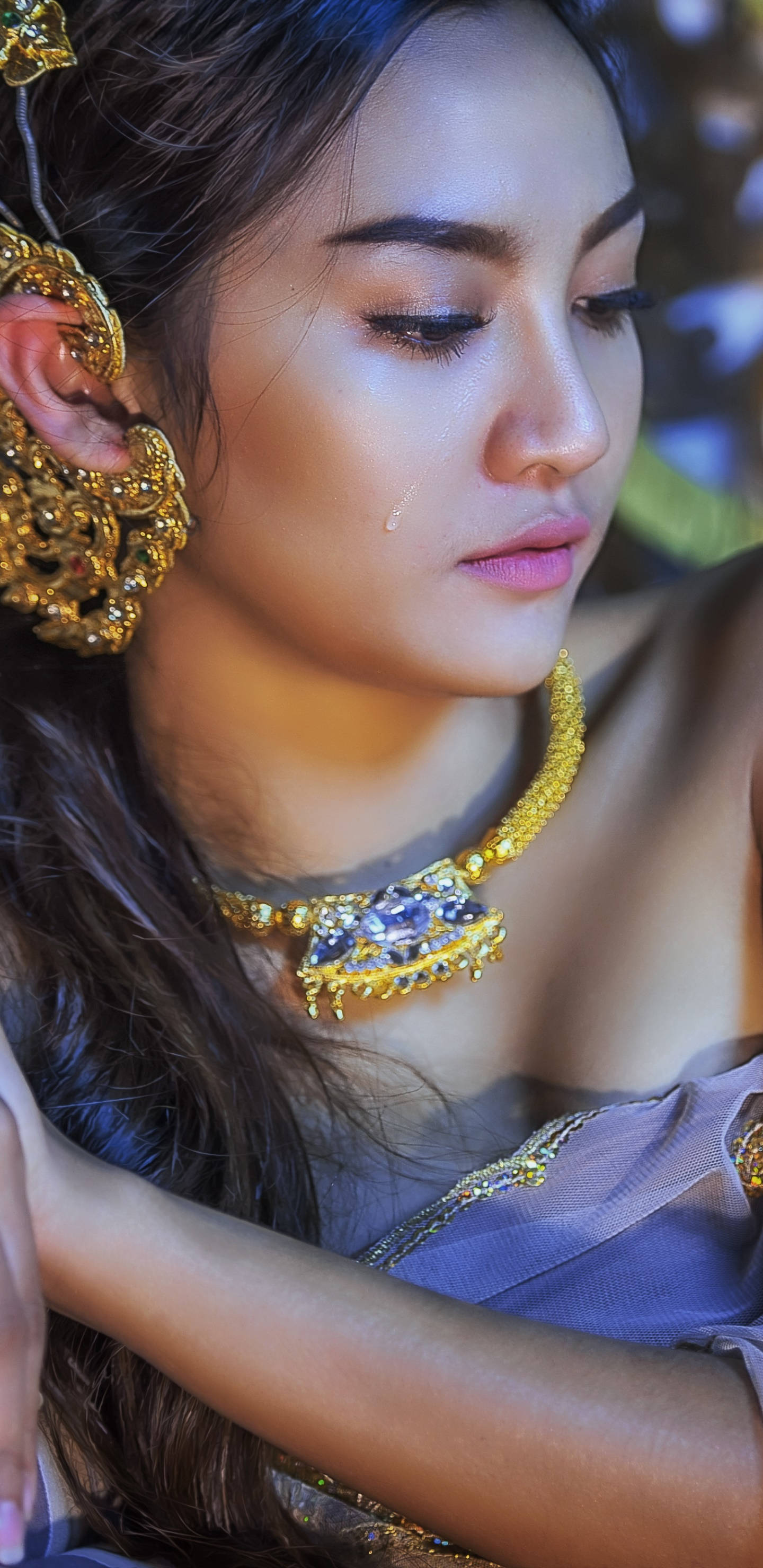 Thailand Woman 桌布 壁紙 — 一個特寫肖像，一位女士佩戴華麗的金飾，淚水從她的眼睛滑落，背景是模糊的花卉。