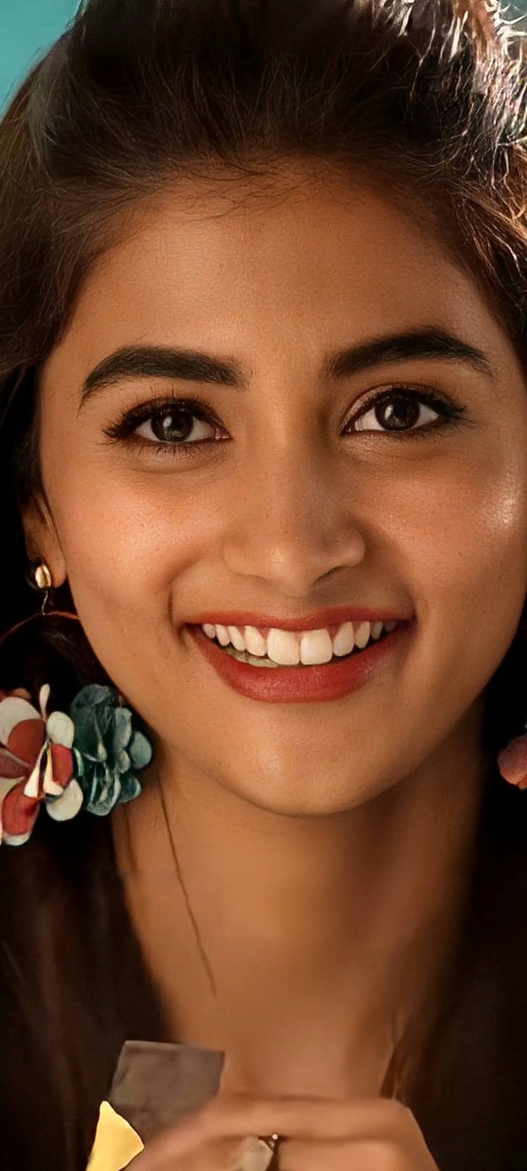 Actress HD 桌布 壁紙 — 一個特寫肖像，一位微笑的年輕女性，深色頭髮，戴著色彩繽紛的花卉耳環，背景是青綠色。