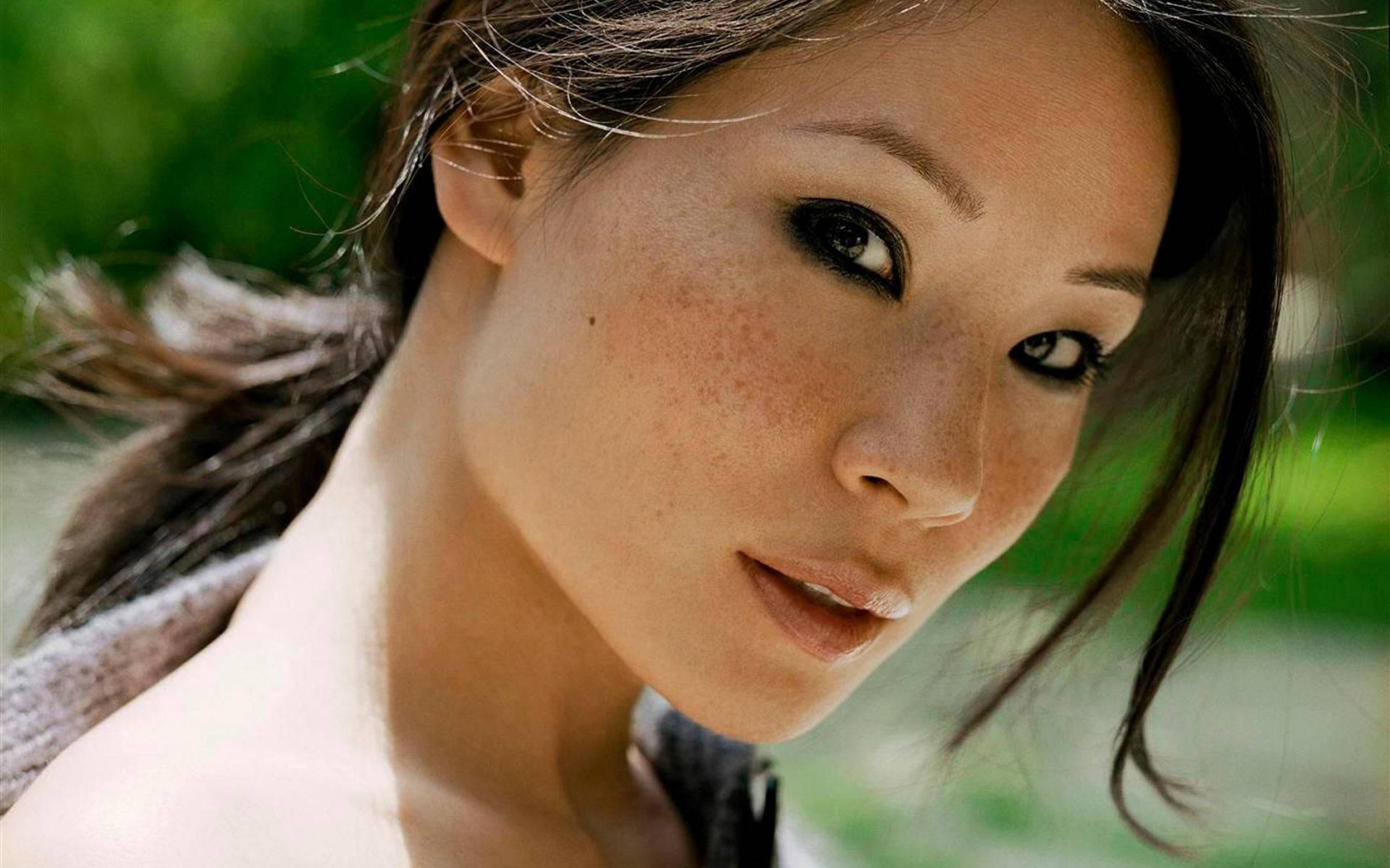 seductive 桌布 壁紙 — 一個特寫肖像，一位擁有深色眼睛和雀斑的女性，在模糊的綠色背景下直視鏡頭。