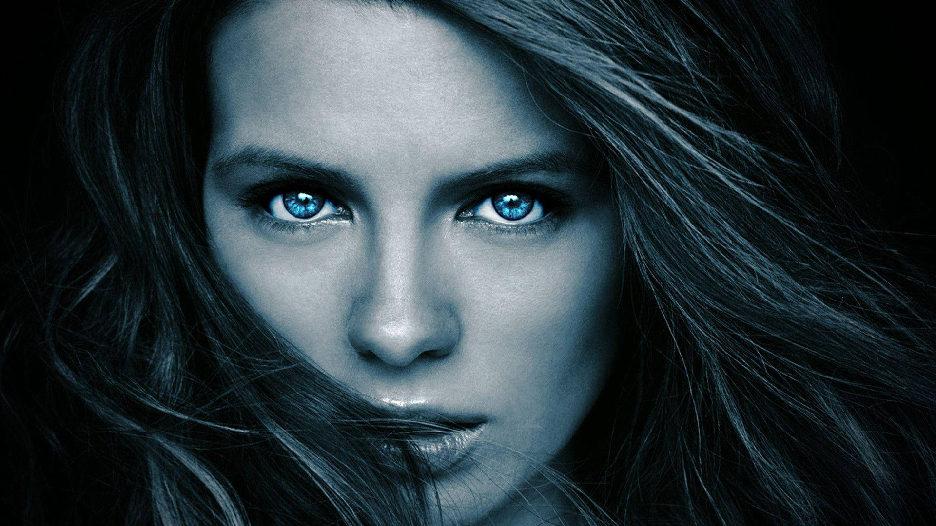 Kate Beckinsale 桌布 壁紙 — 一個特寫肖像，一位擁有銳利藍眼睛和深色頭髮的女性，背景為黑色。