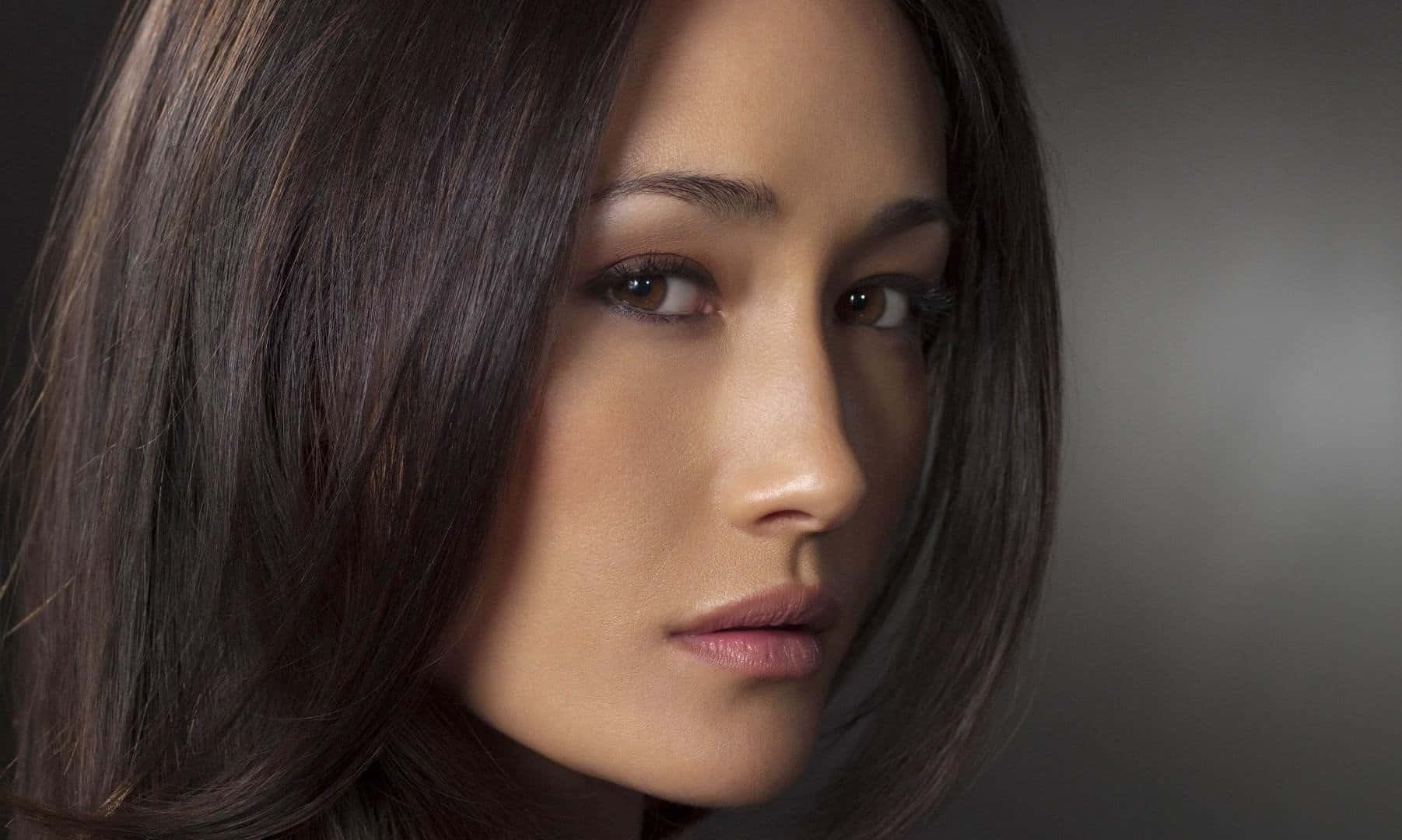 maggie q 桌布 壁紙 — 一個特寫肖像，一位深色頭髮、眼神強烈的女性，背景是柔和的灰色。