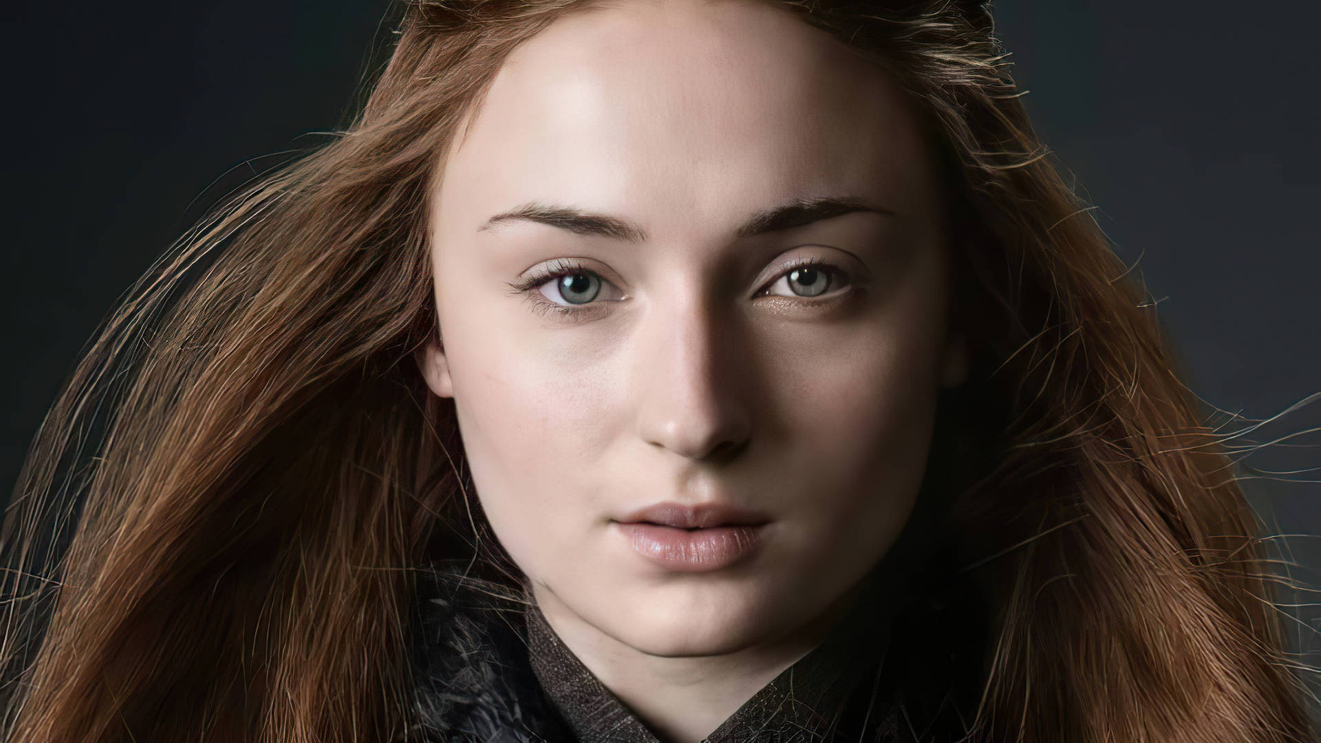 Sansa Stark 桌布 壁紙 — 一個特寫肖像，一位長著赤褐色長髮和深邃藍眼睛的女性在黑暗背景下直視觀眾。