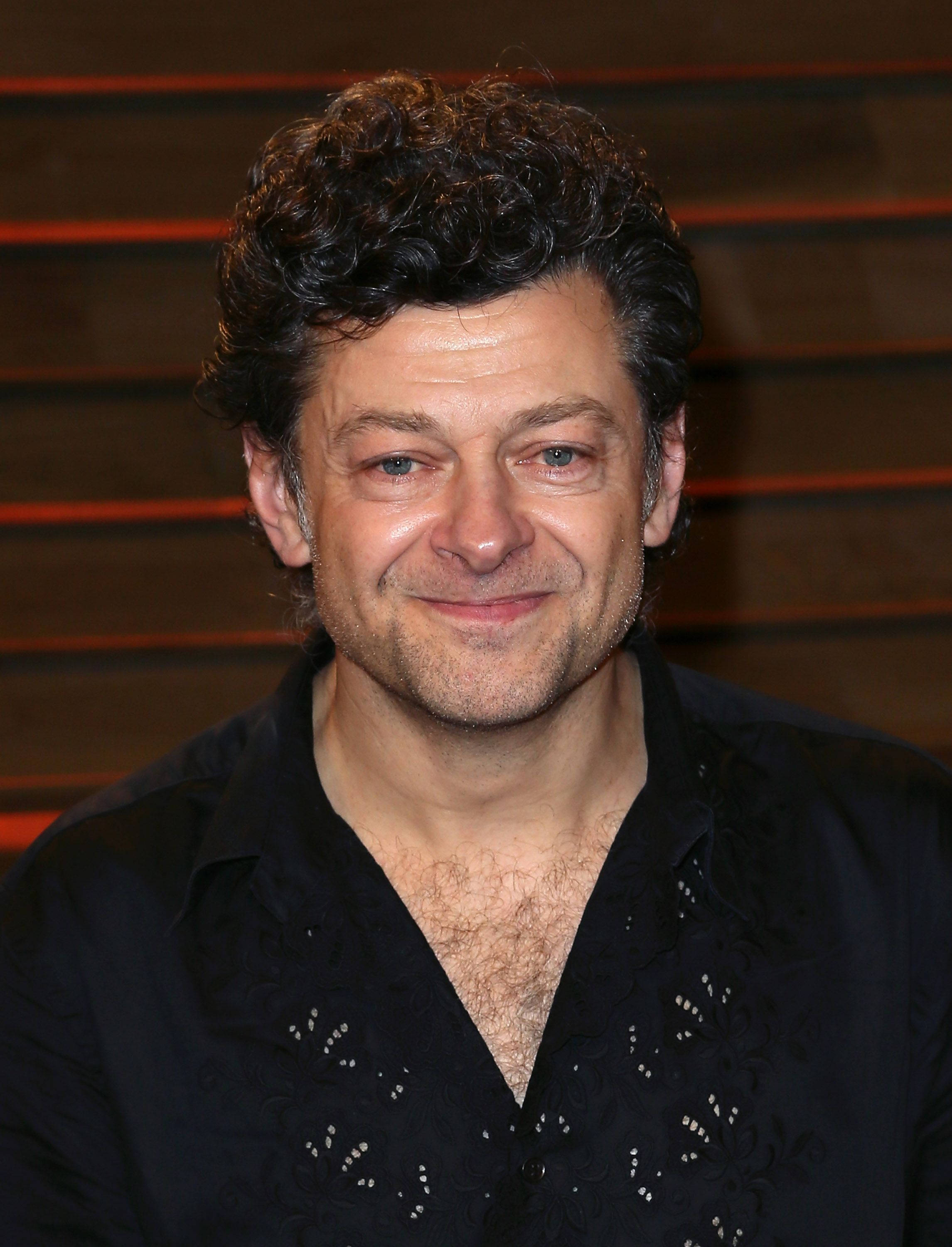 actor 桌布 壁紙 — 一個特寫肖像，一個擁有捲曲深色頭髮和溫暖笑容的男人，穿著黑色圖案襯衫，背景是木條。