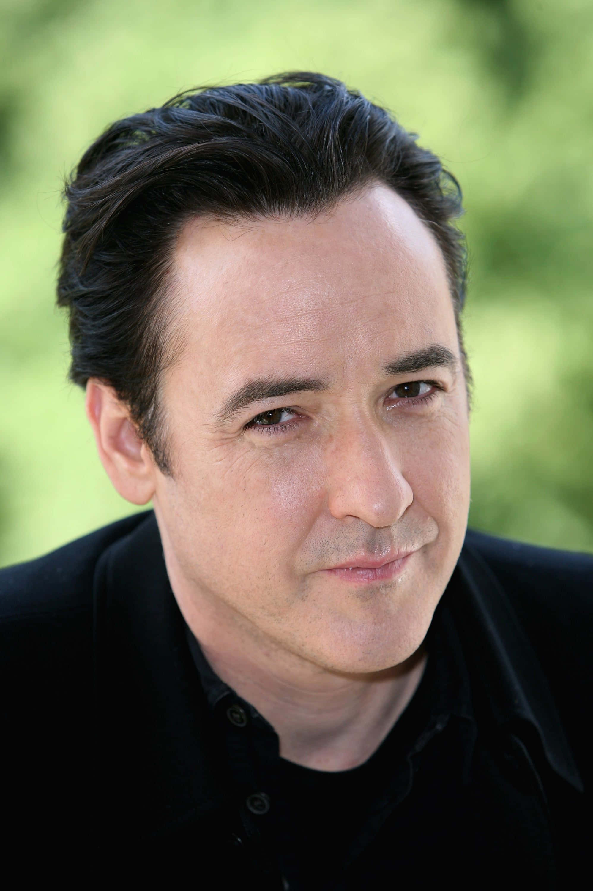 John Cusack 桌布 壁紙 — 一個特寫肖像，一個深色頭髮、帶著微妙微笑的男人，背景是柔和的綠色模糊效果。