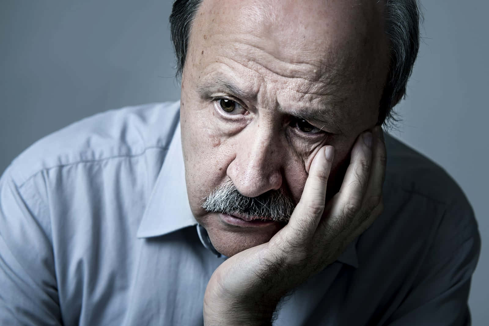 Depressed 桌布 壁紙 — 一個特寫肖像，一個疲憊的中年男人留著鬍子，將頭靠在手上，背景為灰色。