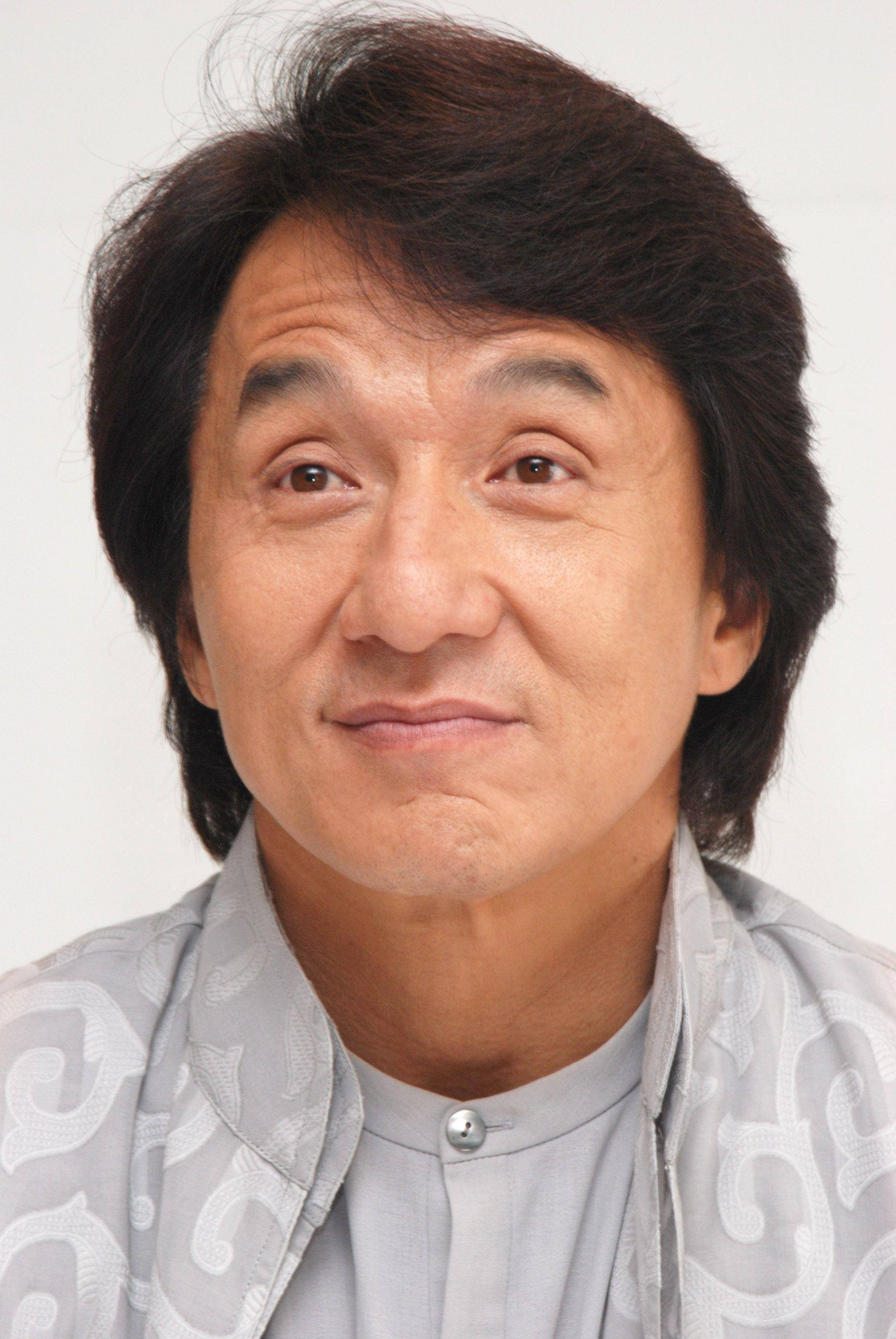 eyebrow raise 桌布 壁紙 — 一個特寫肖像，一名深色頭髮、帶著溫柔微笑的男子，穿著灰色圖案襯衫，背景為純白色。