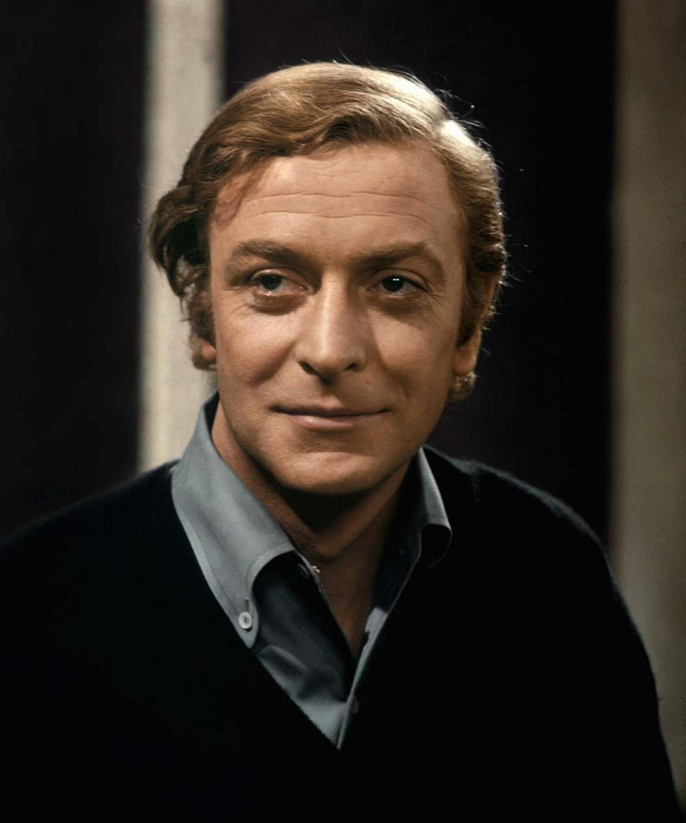 actor 桌布 壁紙 — 一個特寫肖像，一名男子擁有波浪形棕色頭髮，穿著深色毛衣內搭淺藍色襯衫，背景為深色。