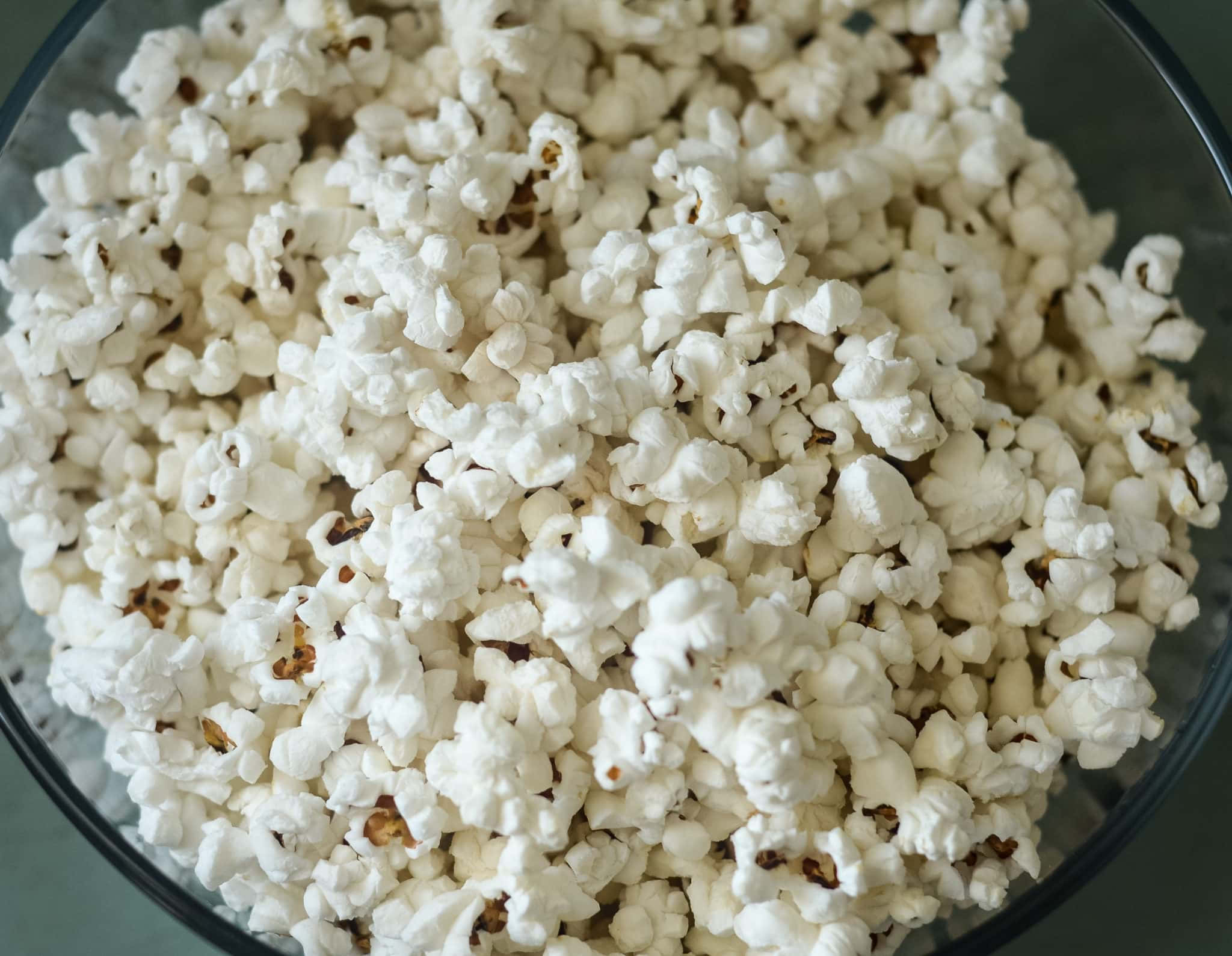 Popcorn 桌布 壁紙 — 一個特寫鏡頭， fluffy 白色爆米花粒帶有棕色斑點，裝滿一個透明玻璃碗。