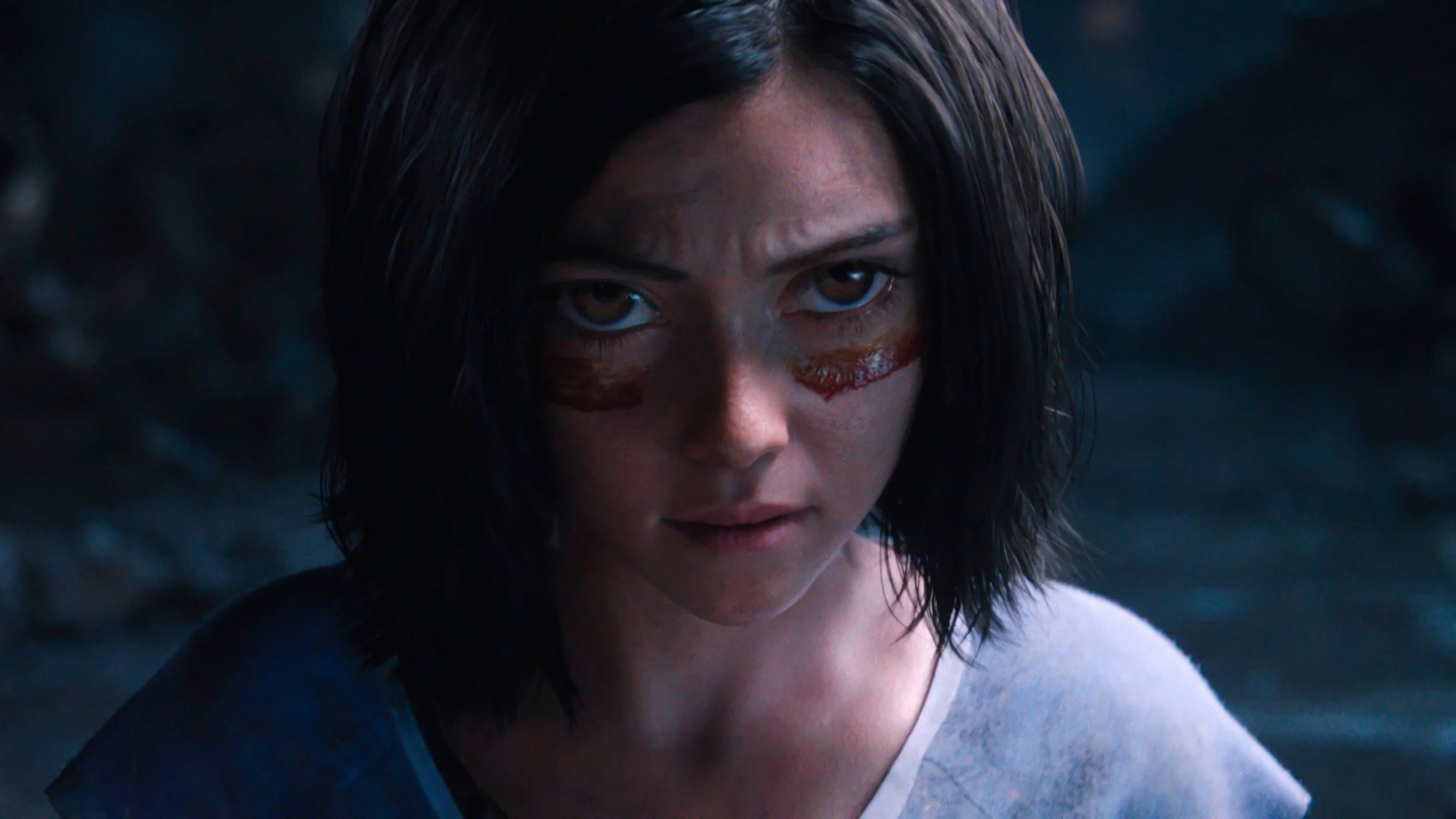 Alita 桌布 壁紙 — 一個特寫鏡頭，一位堅定的年輕女性，深色頭髮，眼睛下方有紅色標記，處於昏暗的藍色照明環境中。