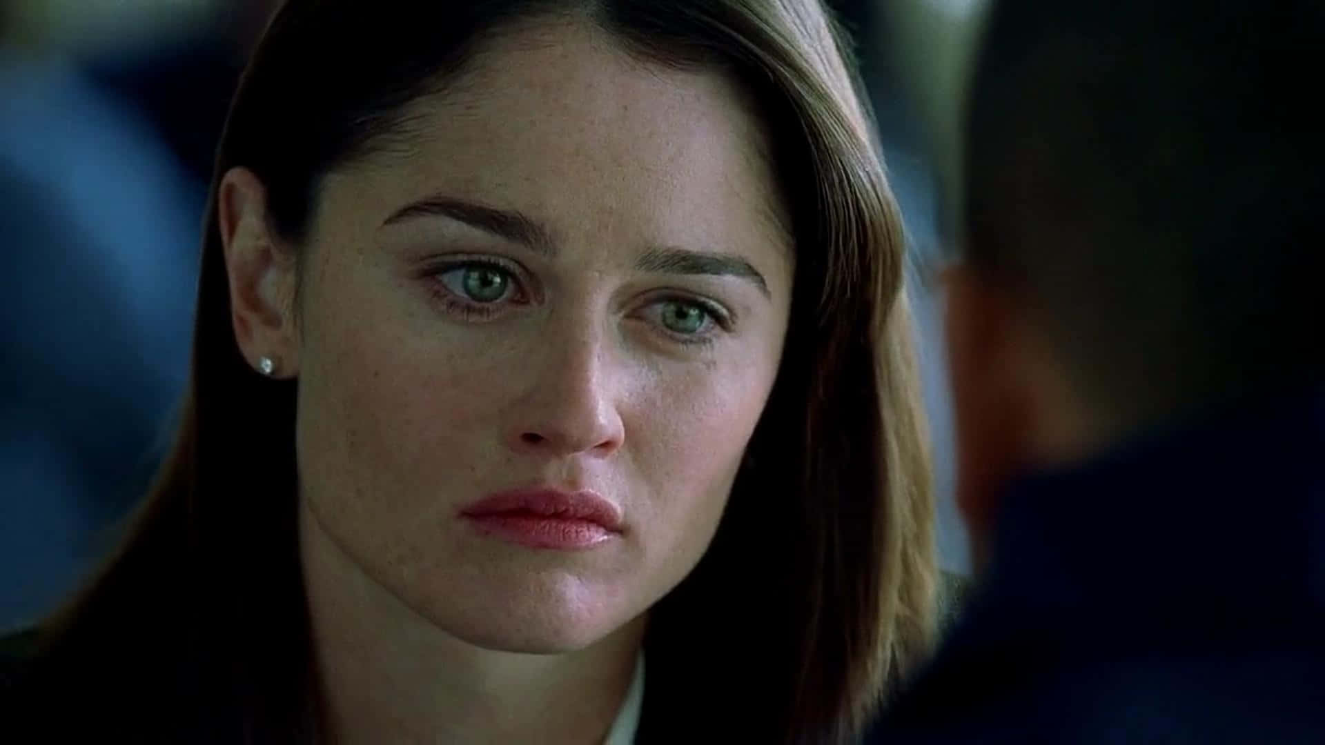 Robin Tunney 桌布 壁紙 — 一個特寫鏡頭，一位擁有綠色眼睛和棕色頭髮的女性在昏暗場景中專注地看著鏡頭外的某人。