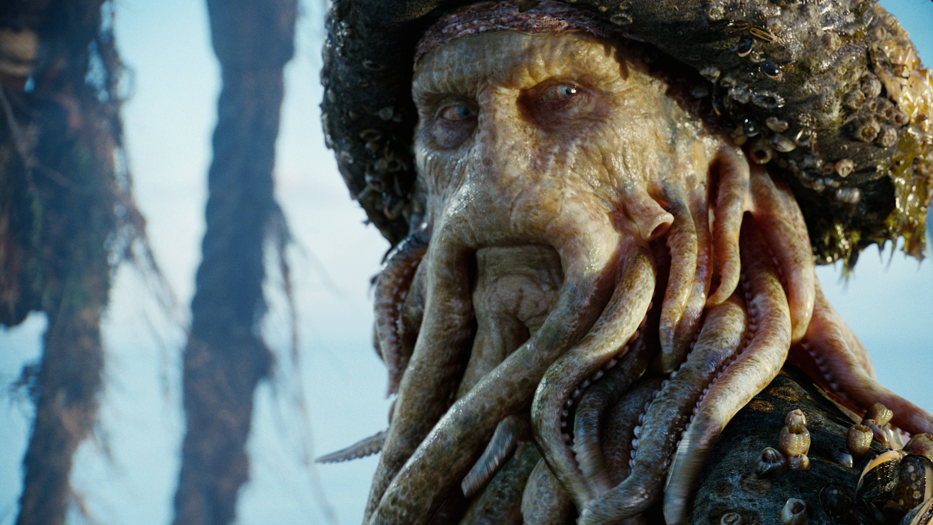 Pirates Of The Caribbean 桌布 壁紙 — 一個特寫鏡頭，一個怪誕的章魚臉海盜，藤壺和海藻依附在他的帽子和觸手上，背景是模糊的海洋。