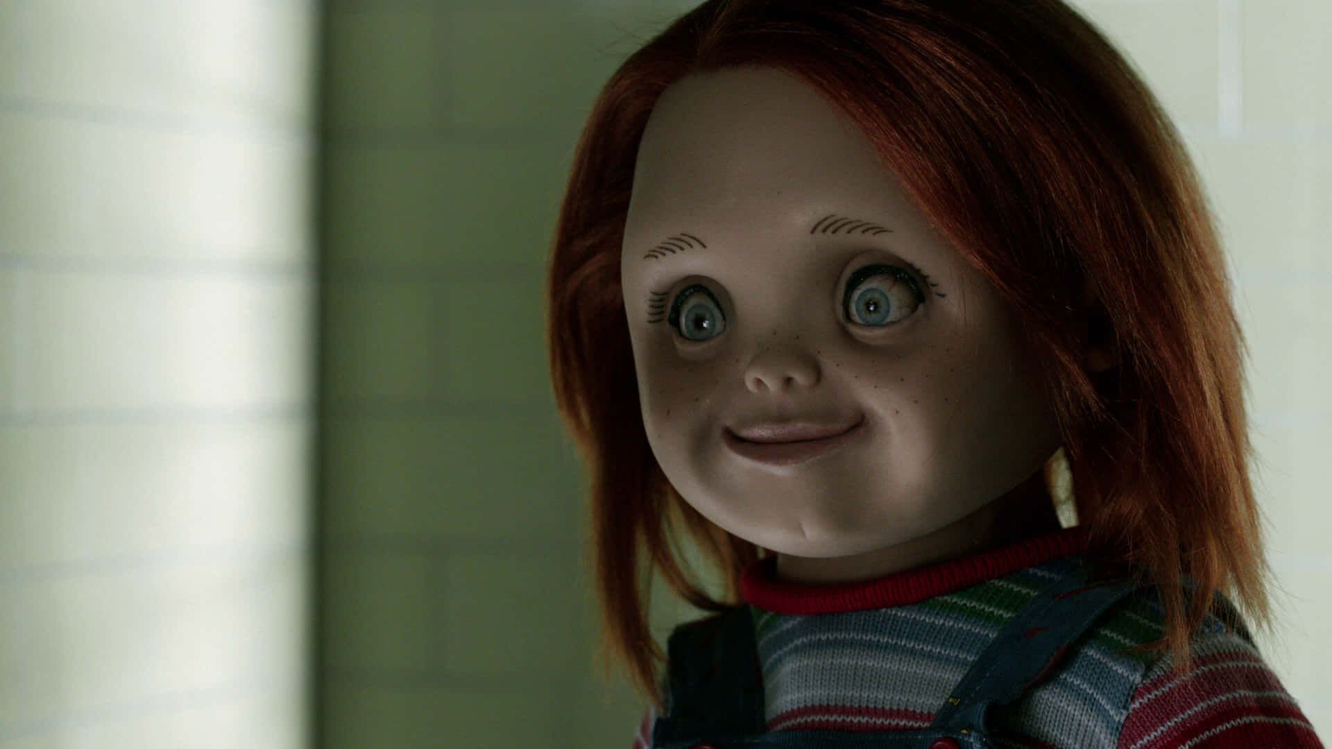 Chucky Doll 桌布 壁紙 — 一個特寫鏡頭，一個紅髮大眼的恐怖娃娃在磁磚浴室裡微笑。