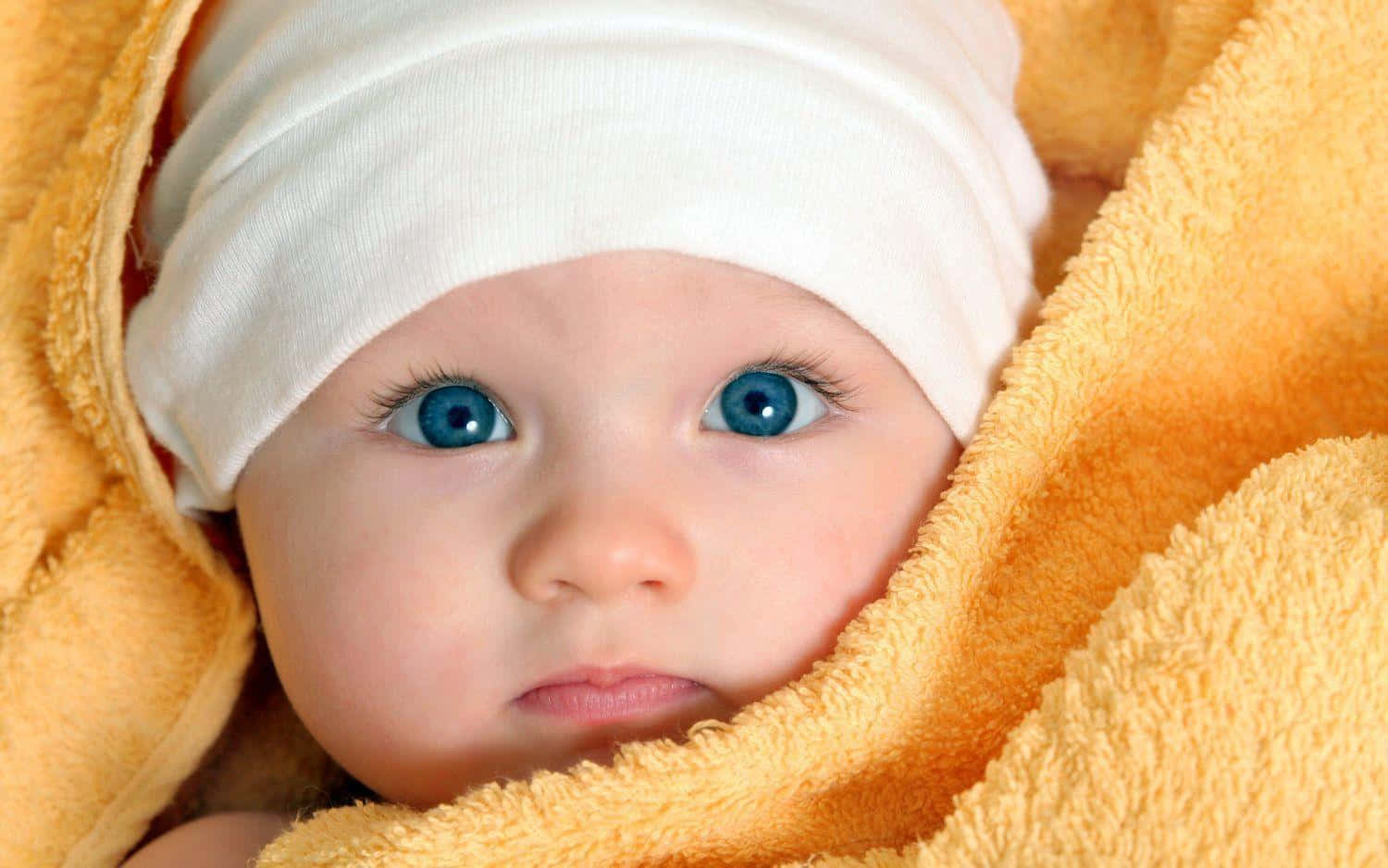 cute baby 桌布 壁紙 — 一個特寫鏡頭，嬰兒用柔軟的黃色毛巾裹著頭，露出一雙引人注目的藍色眼睛。