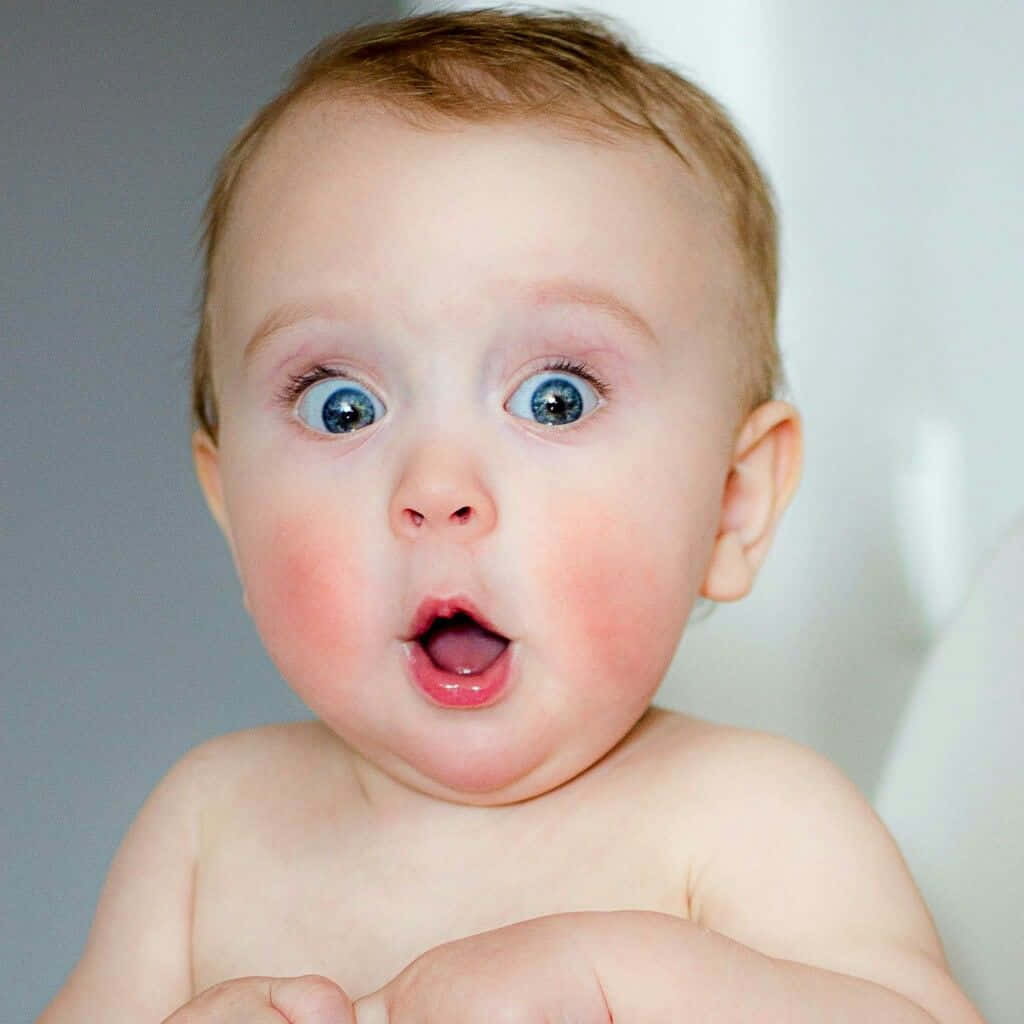 shocked face 桌布 壁紙 — 一個特寫鏡頭，嬰兒睜大藍色眼睛，張開嘴巴，表情驚訝，背景是柔和的灰色。