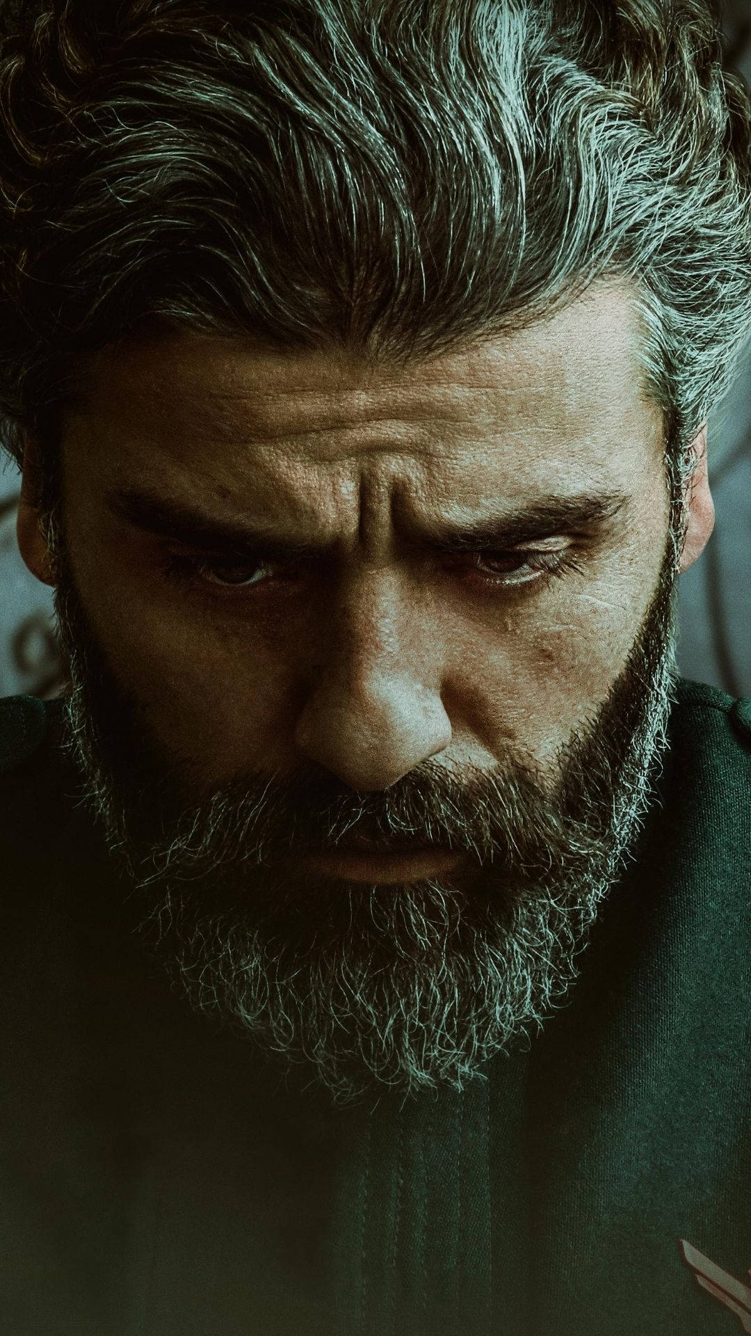 oscar 桌布 壁紙 — 一個特寫鏡頭，展示一位滿頭灰髮、面容滄桑、鬍鬚花白的男子，在昏暗燈光下專注地向下凝視。