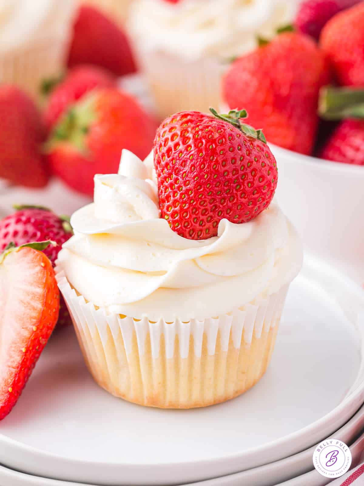 Cupcake 桌布 壁紙 — 一個特寫鏡頭，展示一個以草莓為配料、帶有奶油白色糖霜的杯子蛋糕，周圍環繞著新鮮的紅色草莓。