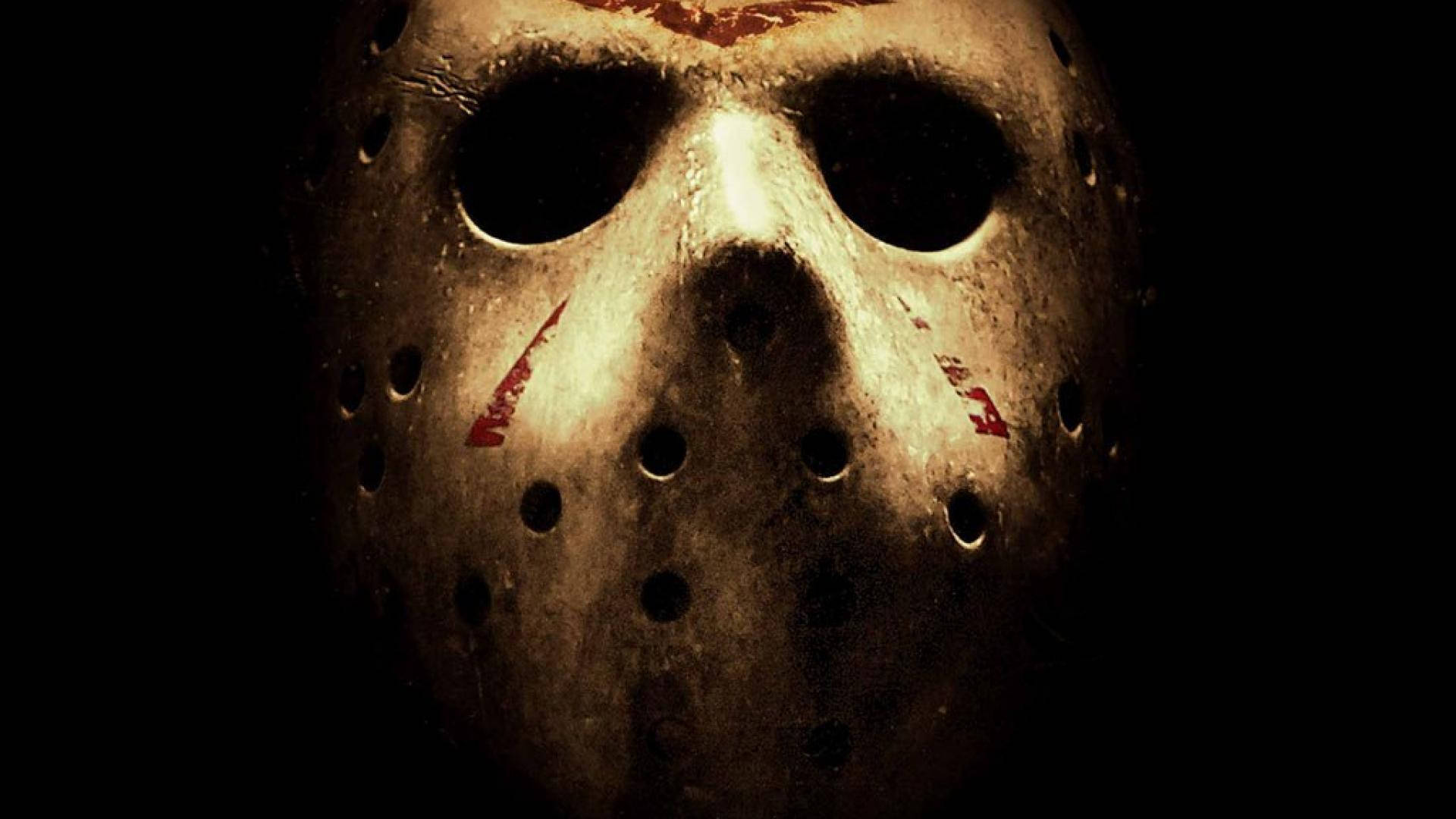horror villains 桌布 壁紙 — 一個特寫鏡頭，展示一個帶有血痕的風化曲棍球面具，由單一燈光照射在黑色背景上。