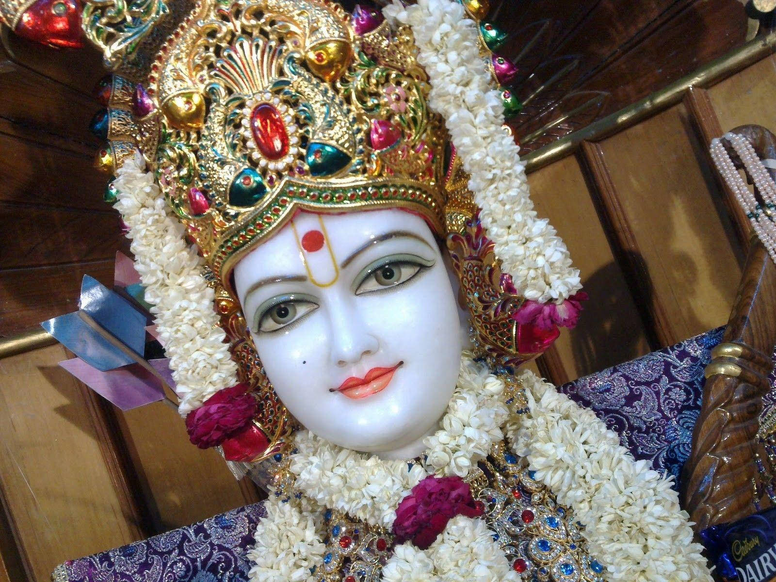 Swaminarayan 桌布 壁紙 — 一個特寫鏡頭，展示一個神聖偶像，飾有寶石皇冠和白色花環，背景為木質。
