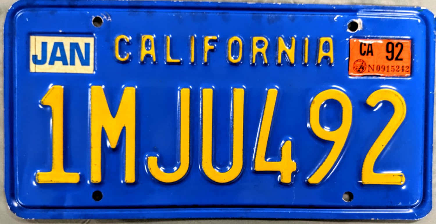 Car License Plate 桌布 壁紙 — 一個特寫鏡頭，展示一塊復古加州車牌，藍色背景上有粗體黃色字母，顯示登記詳情。
