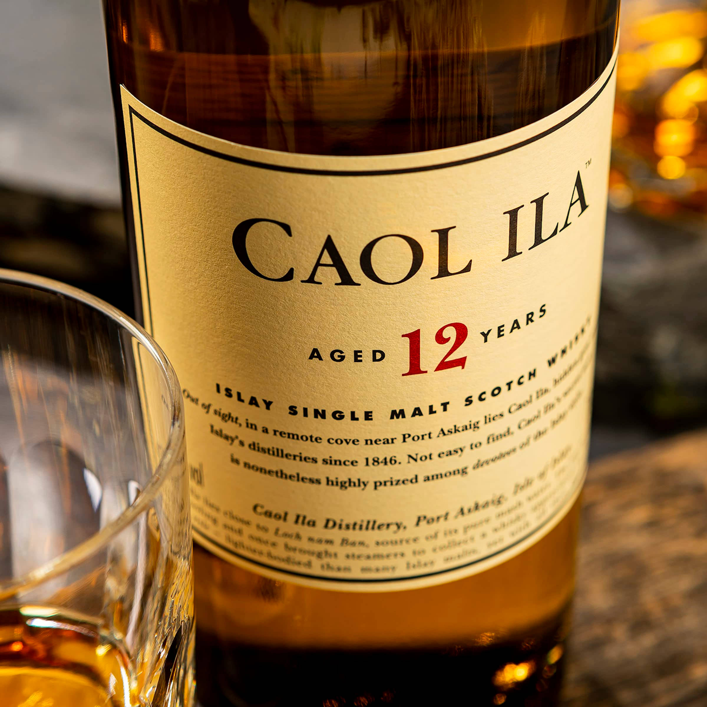 alcohol 桌布 壁紙 — 一個特寫鏡頭，展示一瓶Caol Ila 12年艾雷島單一麥芽蘇格蘭威士忌，旁邊放著一個裝有琥珀色液體的玻璃杯，置於木質表面上。