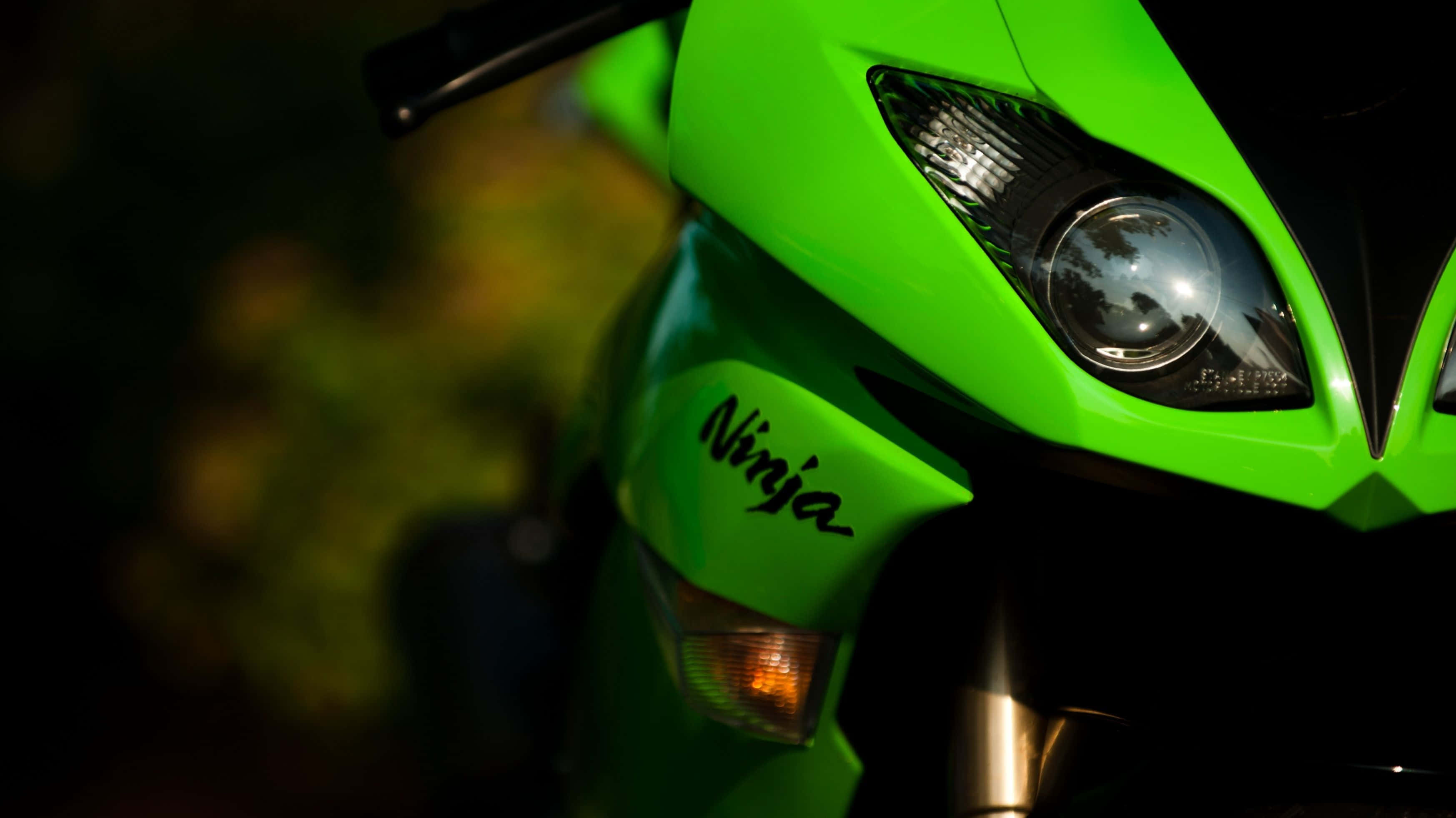 Kawasaki Desktop 桌布 壁紙 — 一個特寫鏡頭，展示一盞充滿活力的綠色Kawasaki Ninja機車頭燈在柔和的金色光芒中，對著模糊的自然背景發光。