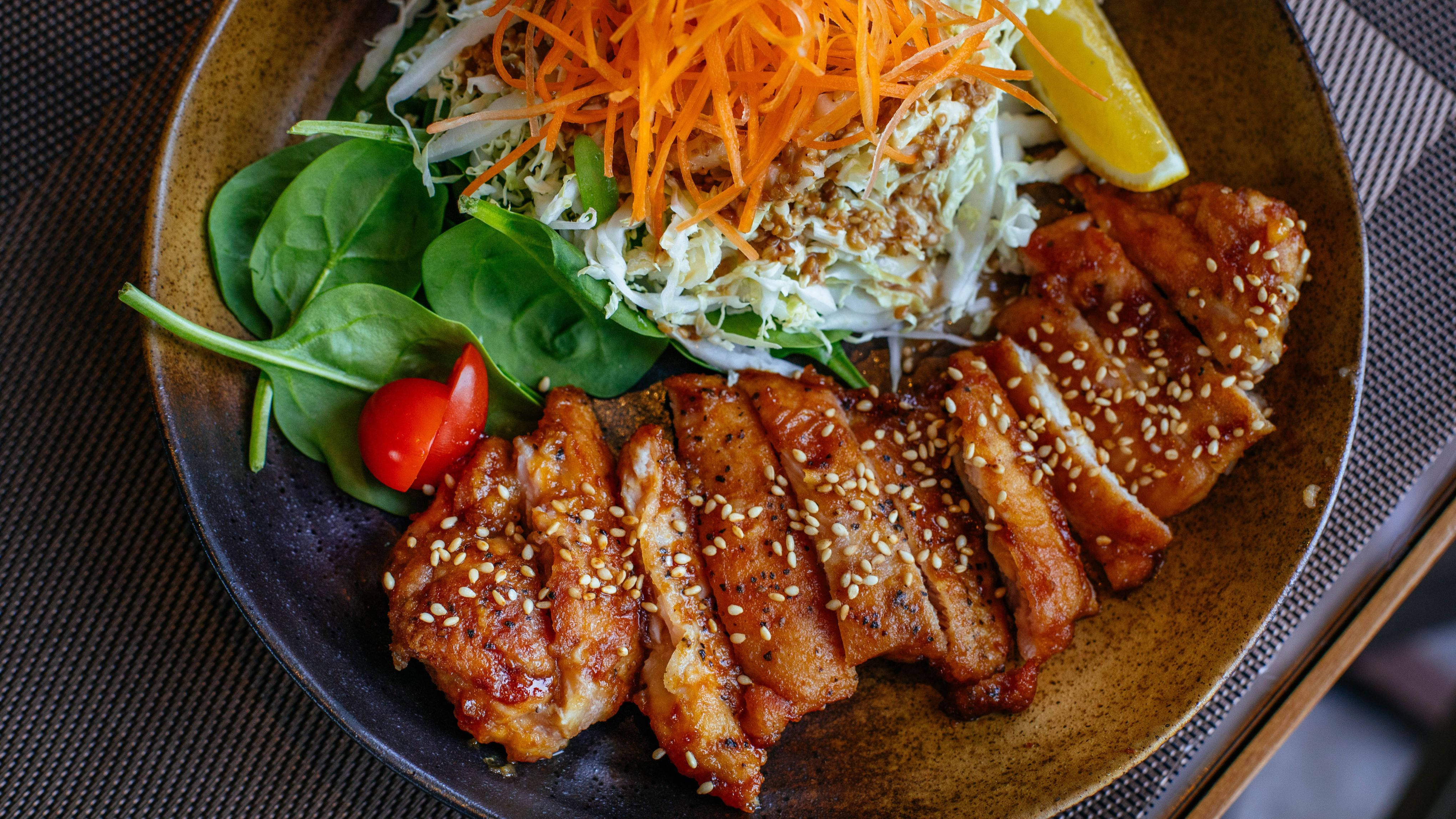 Food 4K 桌布 壁紙 — 一個特寫鏡頭，展示一碗美味的照燒雞肉，上面鋪滿了刨絲紅蘿蔔、高麗菜、芝麻和檸檬角。