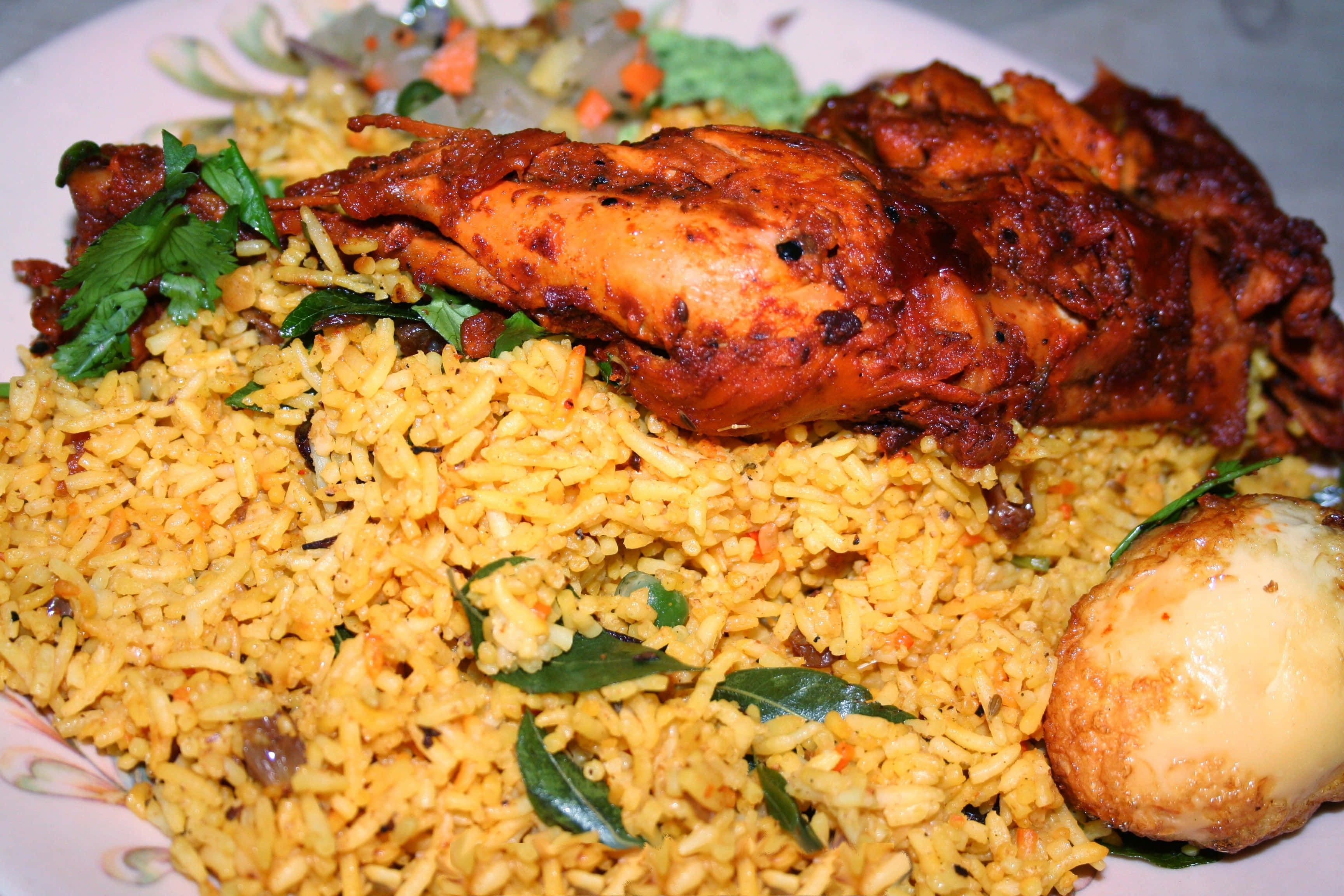 Biryani 桌布 壁紙 — 一個特寫鏡頭，展示一碟金黃色米飯、香料雞肉和一個水煮蛋，並以新鮮咖哩葉點綴。