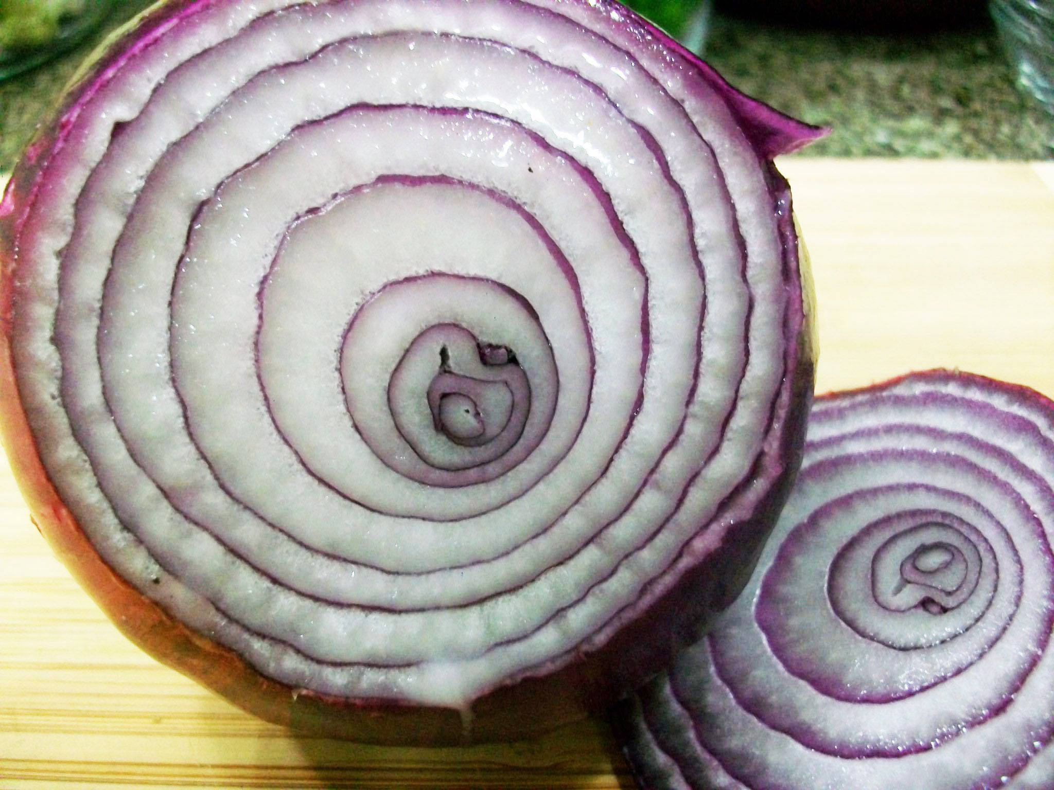 sliced 桌布 壁紙 — 一個特寫鏡頭，展示切開的紅洋蔥在木砧板上顯露出複雜的同心紫色和白色環紋。