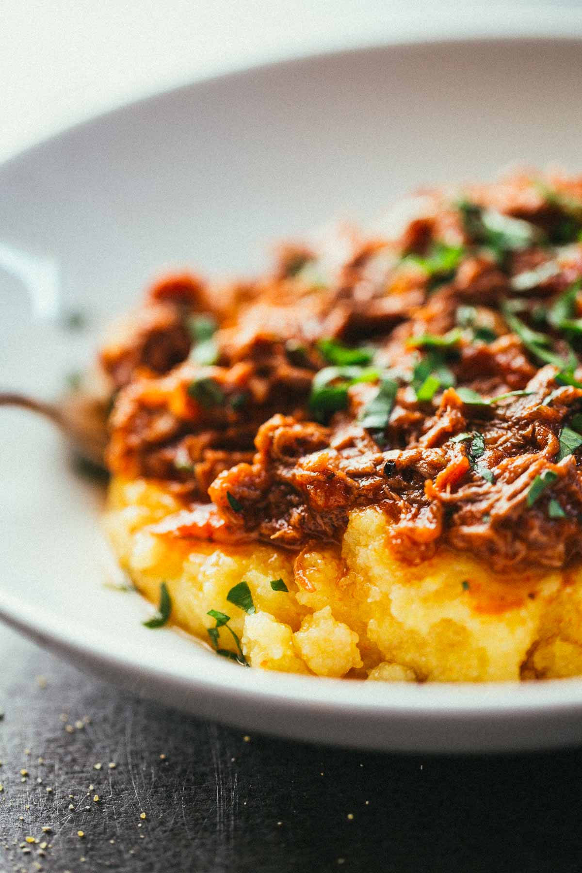 Food Photography 桌布 壁紙 — 一個特寫鏡頭，展示白色碗中嫩滑的肉絲配上濃郁醬汁，放在 creamy 的黃色玉米糊上，並以新鮮綠色香草點綴。