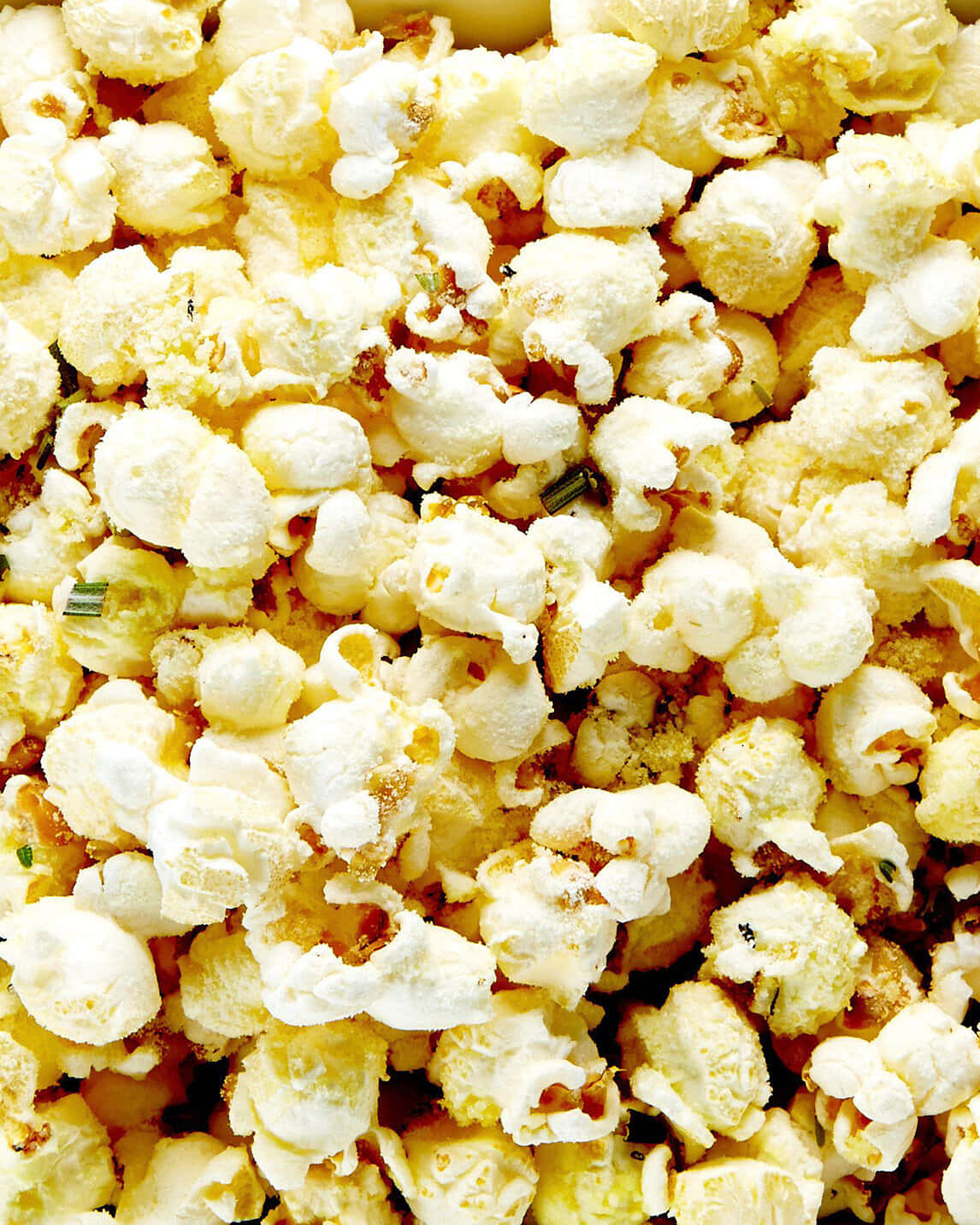 Popcorn 桌布 壁紙 — 一個特寫鏡頭，展示鬆軟的奶油爆米花，上面撒有綠色香草和金黃色的調味料。