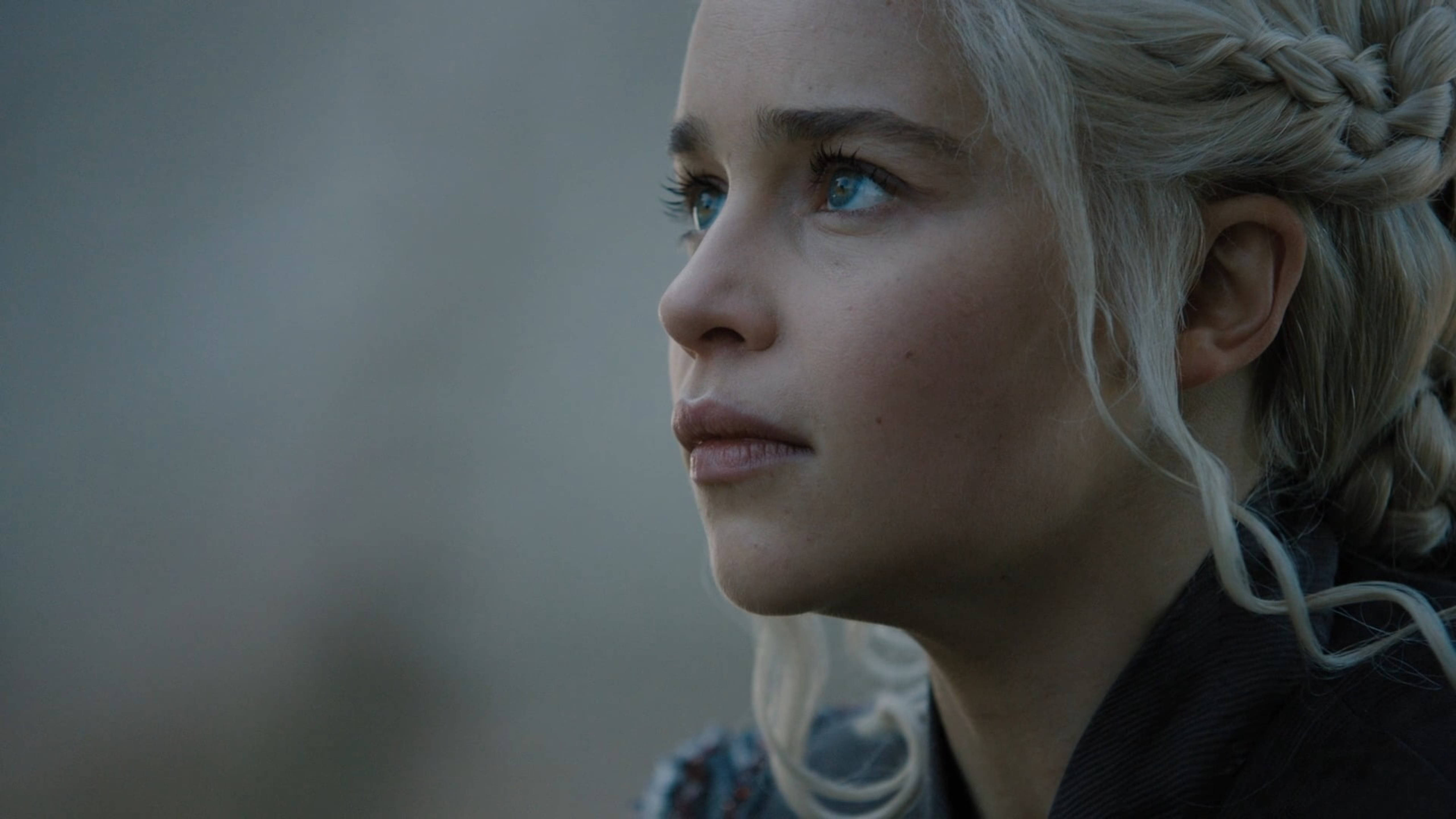 daenerys 桌布 壁紙 — 一個特寫鏡頭，捕捉一位編織金髮、擁有銳利藍眼的女性，若有所思地凝視遠方。