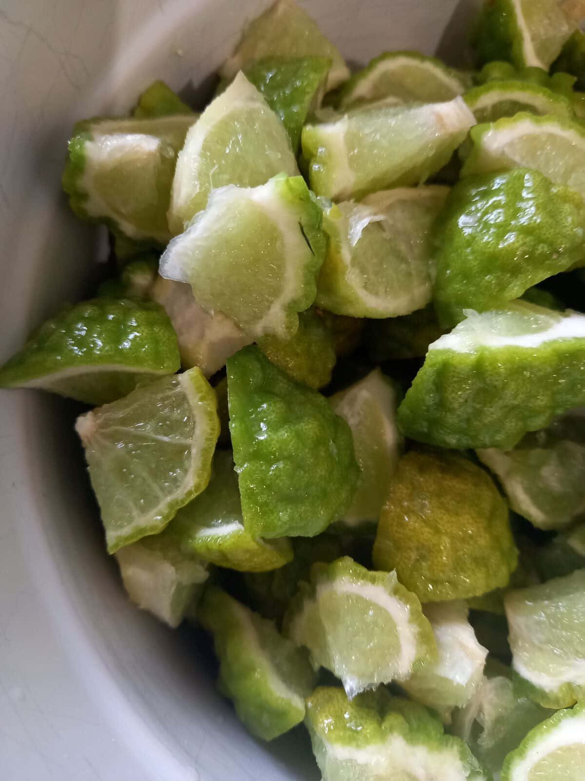 citrus 桌布 壁紙 — 一個特寫鏡頭，新鮮切碎的青檸，帶有紋理的果皮和多汁的果肉，堆放在一個白色碗中。