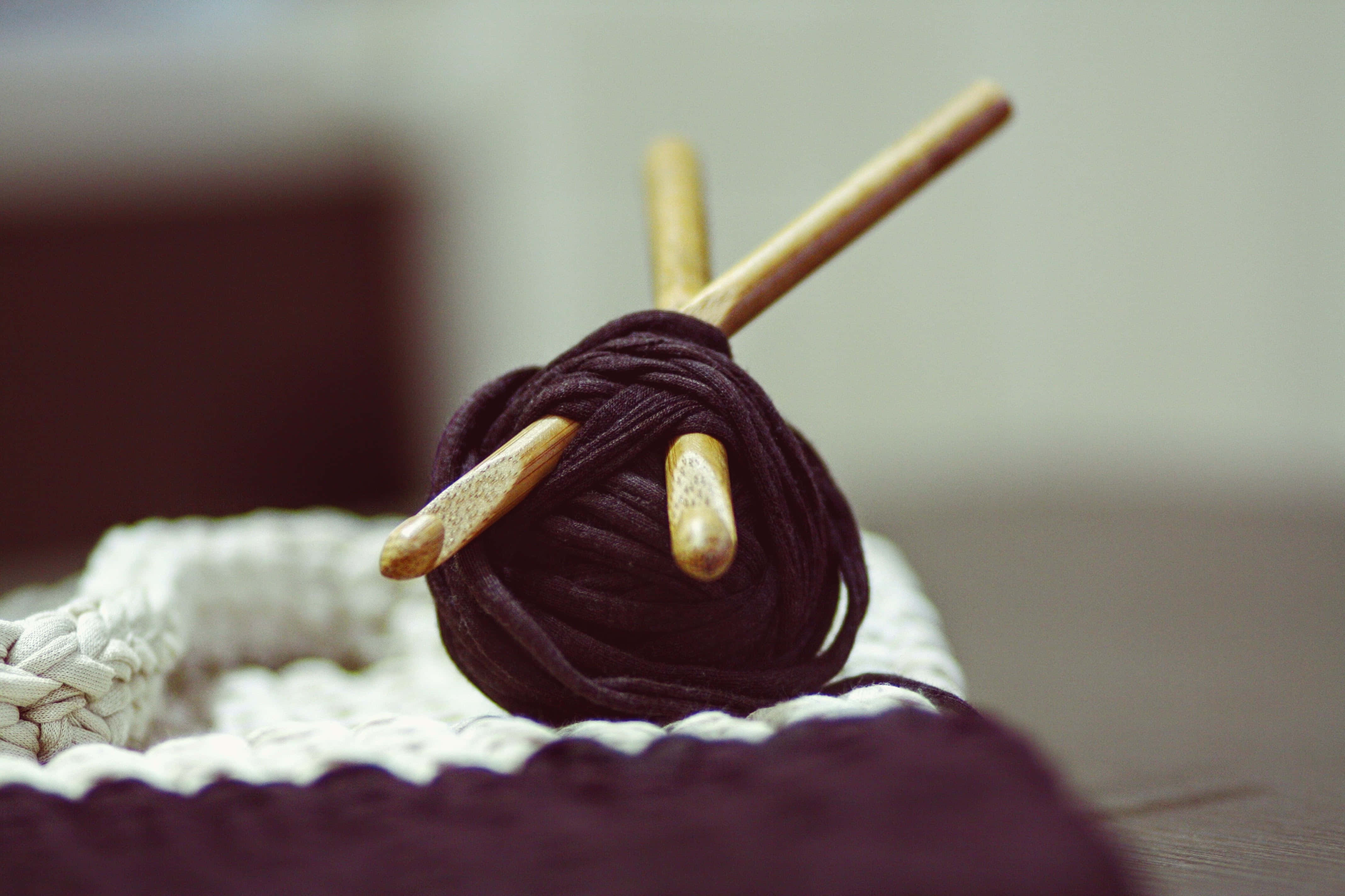 Knitting 桌布 壁紙 — 一個特寫鏡頭，木製鉤針放在深色毛線球上，下方是白色鉤針作品，背景柔和模糊。