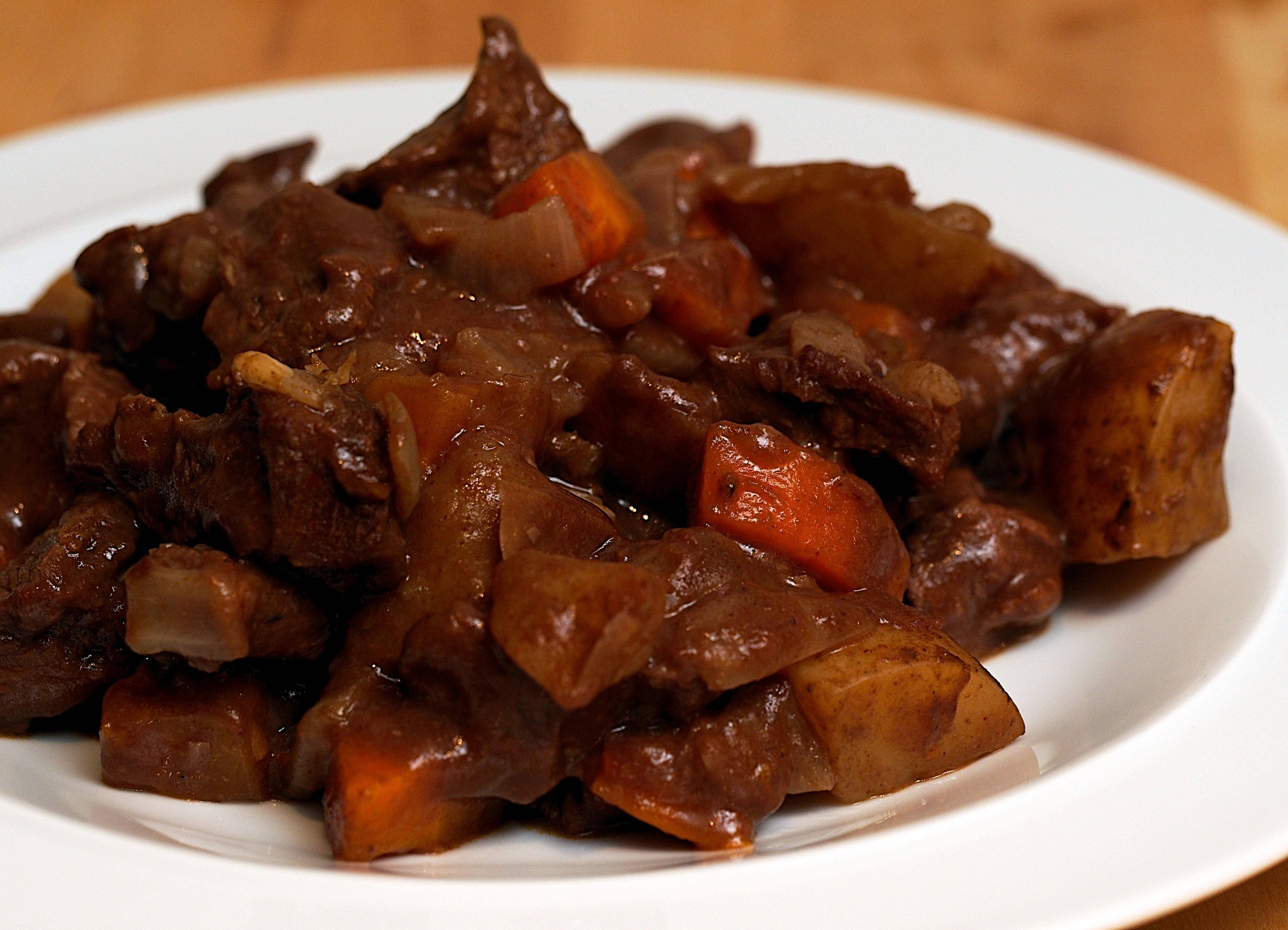 meat 桌布 壁紙 — 一個特寫鏡頭，白盤上盛載著濃郁的褐色燉牛肉，搭配紅蘿蔔和馬鈴薯，冒著蒸氣。