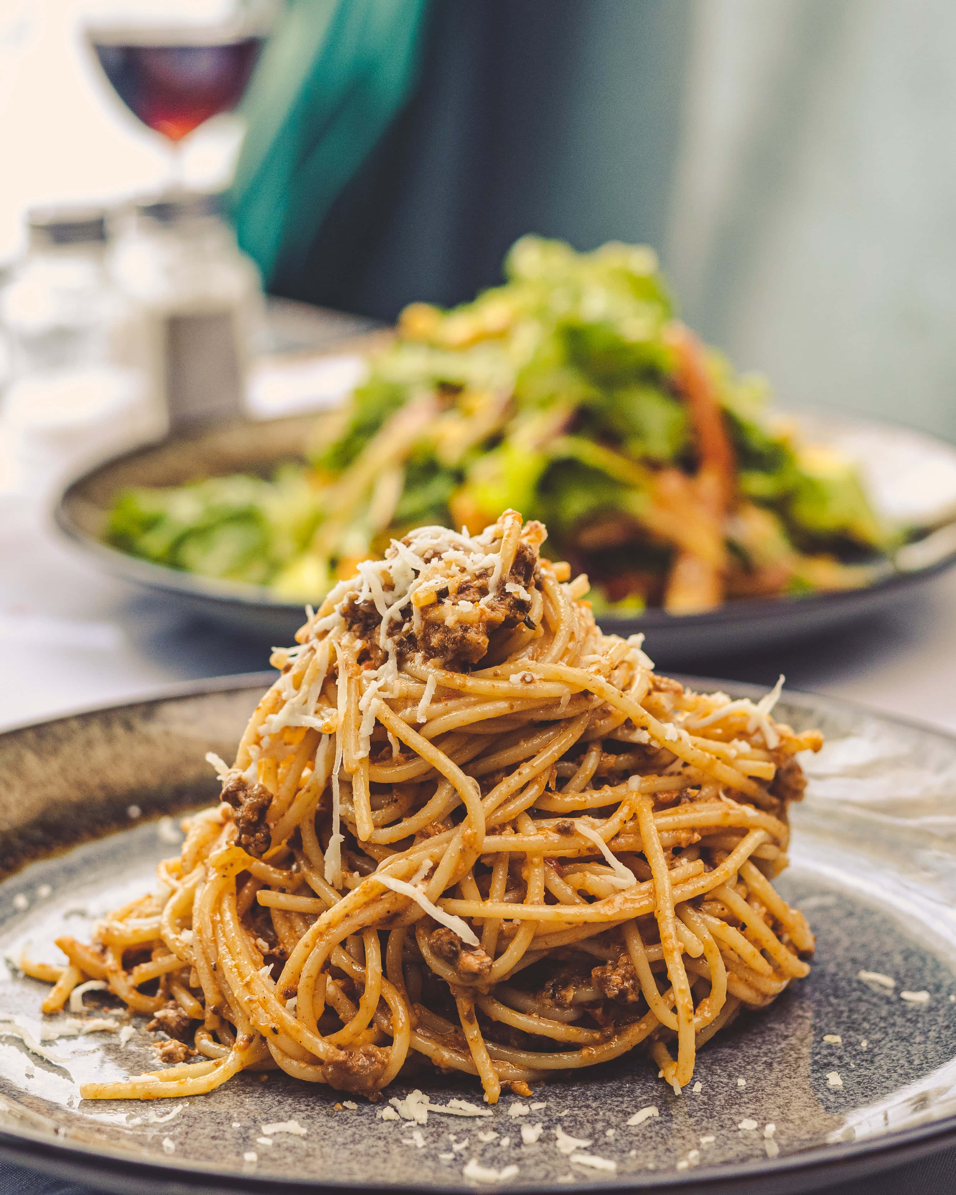 Noodles 桌布 壁紙 — 一個特寫鏡頭，義大利肉醬麵高高堆在一個質樸的盤子上，配上磨碎的起司和一份沙拉，背景柔和。