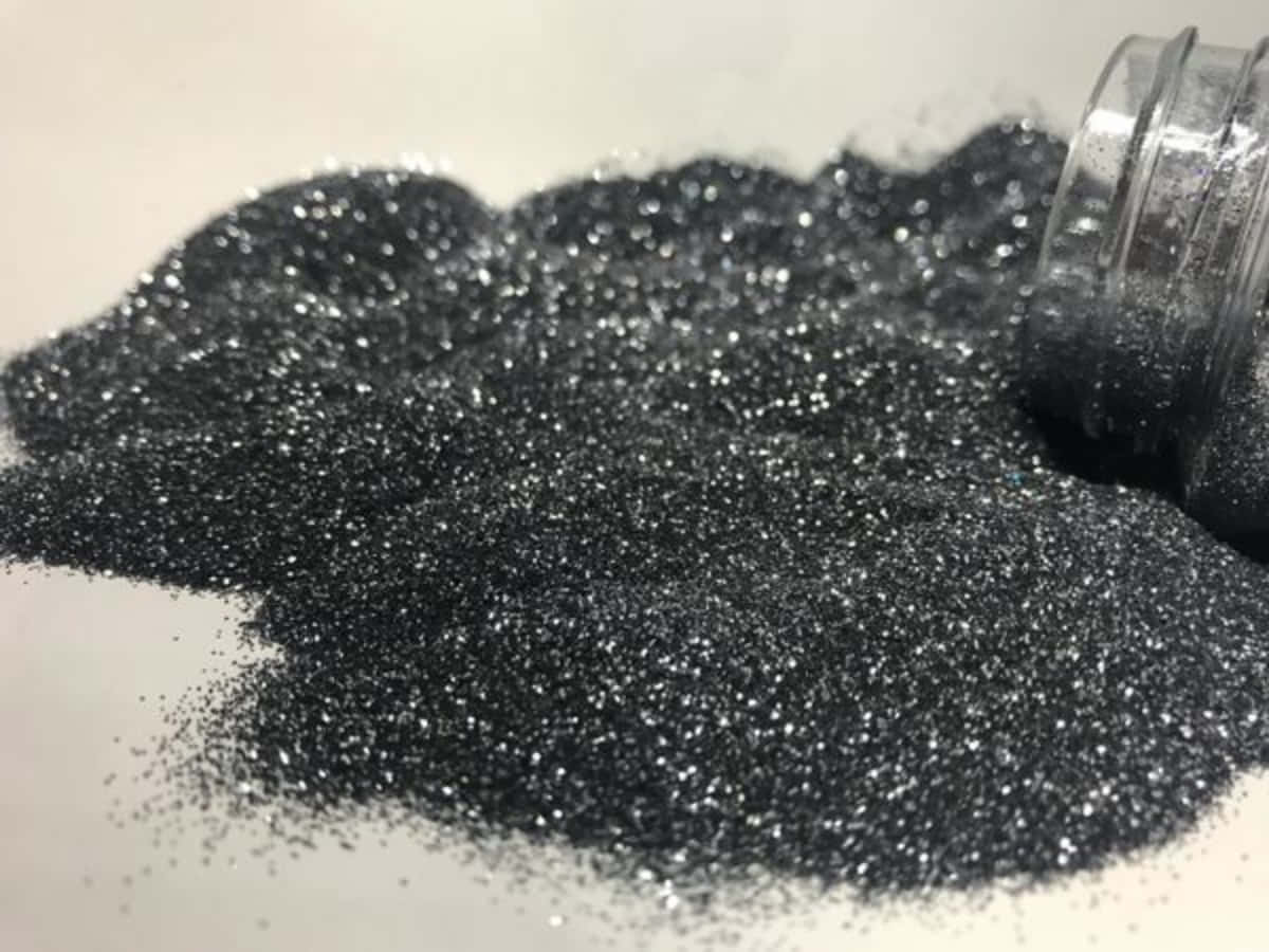 Black Powder 桌布 壁紙 — 一個特寫鏡頭，閃亮的黑色亮粉從透明罐子灑落到白色表面上。