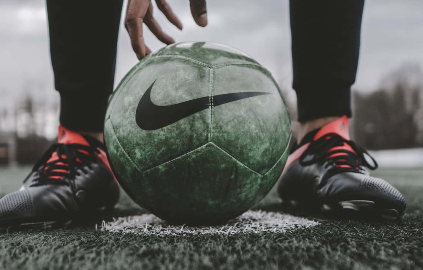 Soccer Ball 桌布 壁紙 — 一個特寫鏡頭，顯示一個經風化的綠色Nike足球正被球員的腳在草地上定位。