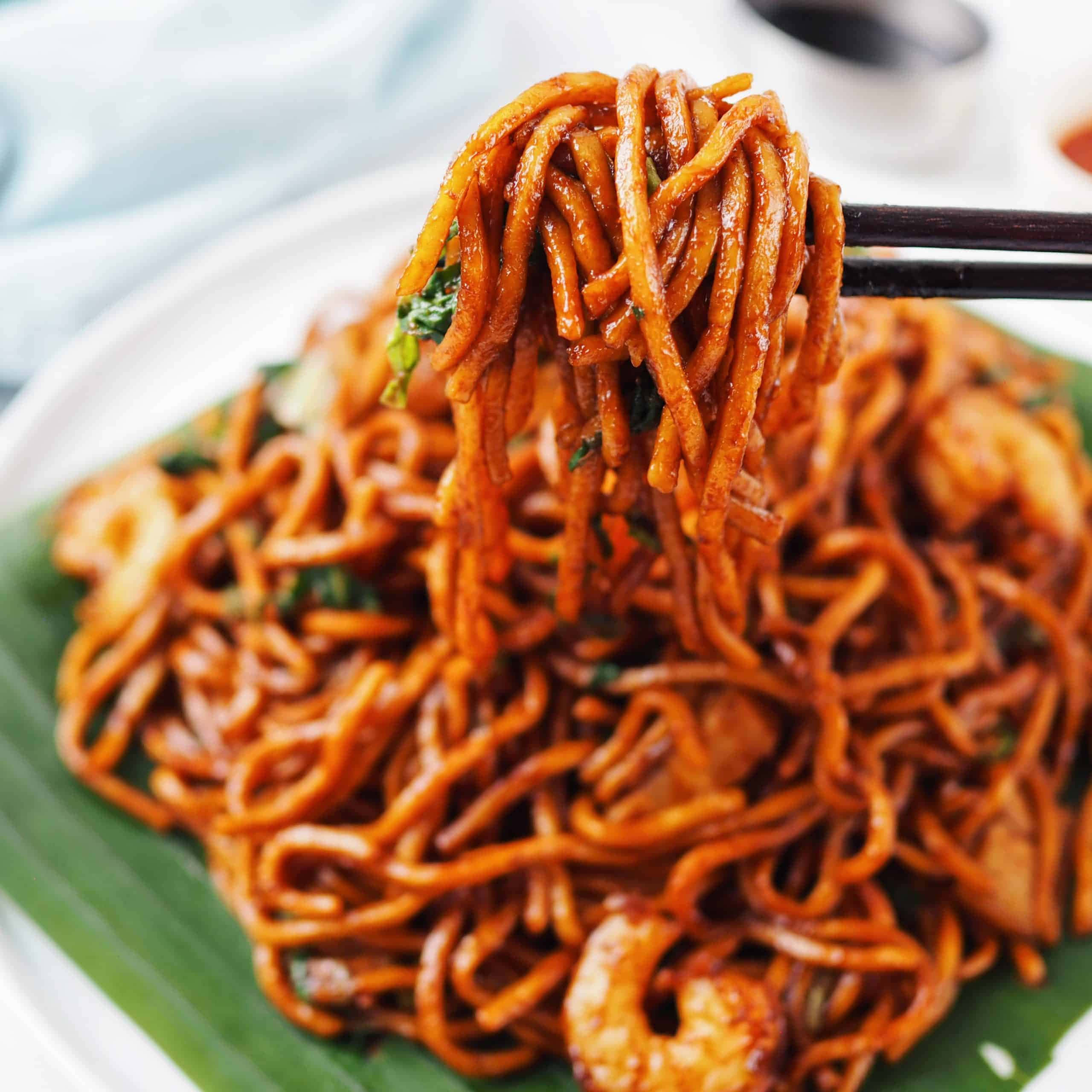 Delicious Food 桌布 壁紙 — 一個特寫鏡頭，顯示光澤的橙色麵條搭配蝦和香草，用筷子夾起放在綠葉上。