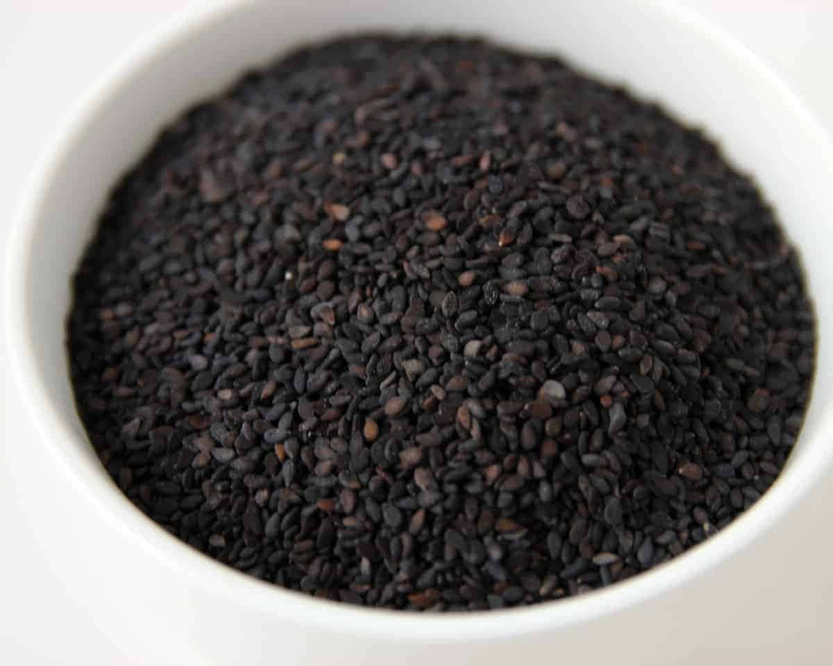 Black Sesame 桌布 壁紙 — 一個特寫鏡頭，顯示光澤的黑芝麻填滿一個白色陶瓷碗，背景是潔淨的白色。