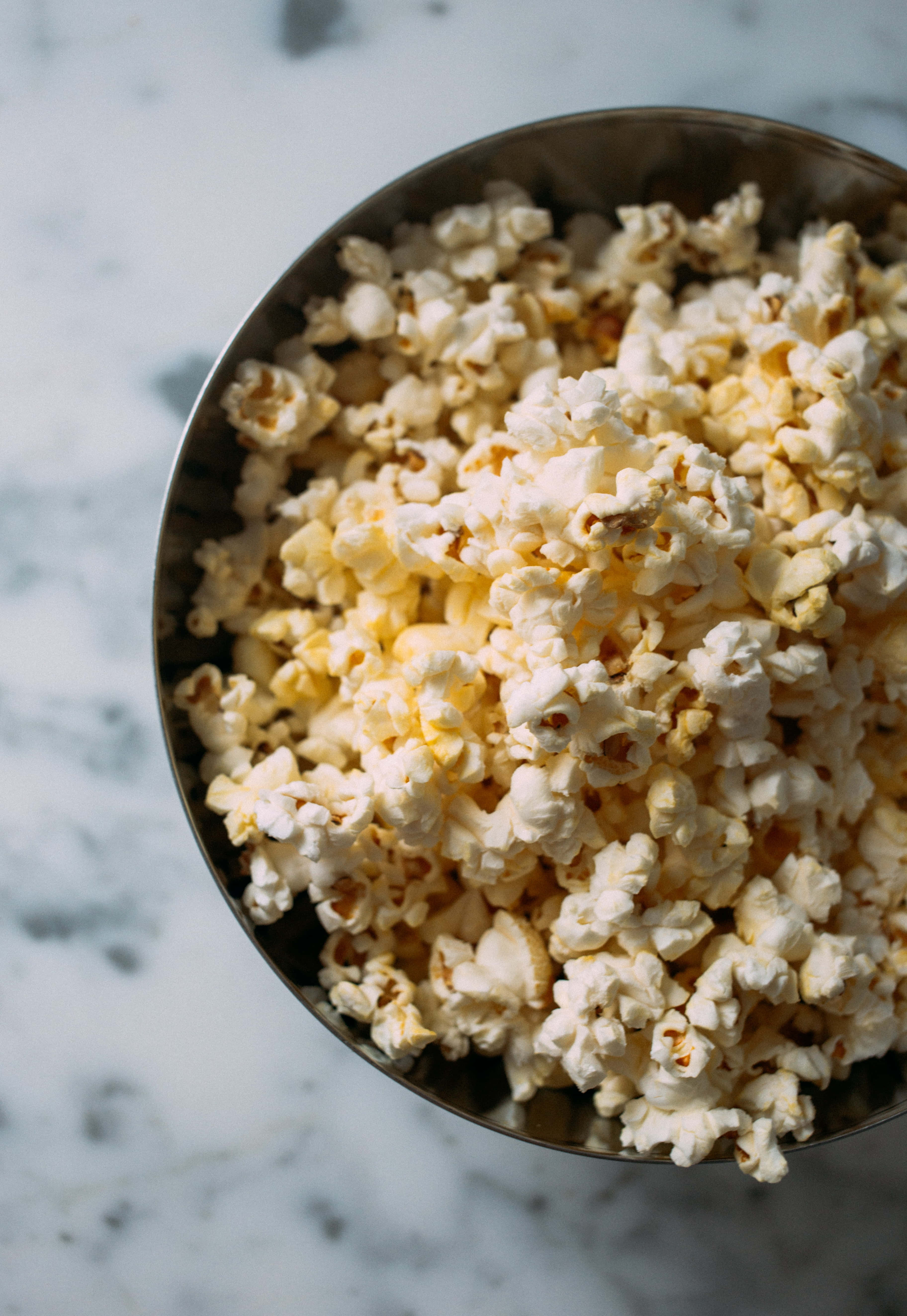 Popcorn 桌布 壁紙 — 一個特寫鏡頭，顯示白色爆米花在金屬碗中溢出，放在大理石表面上。