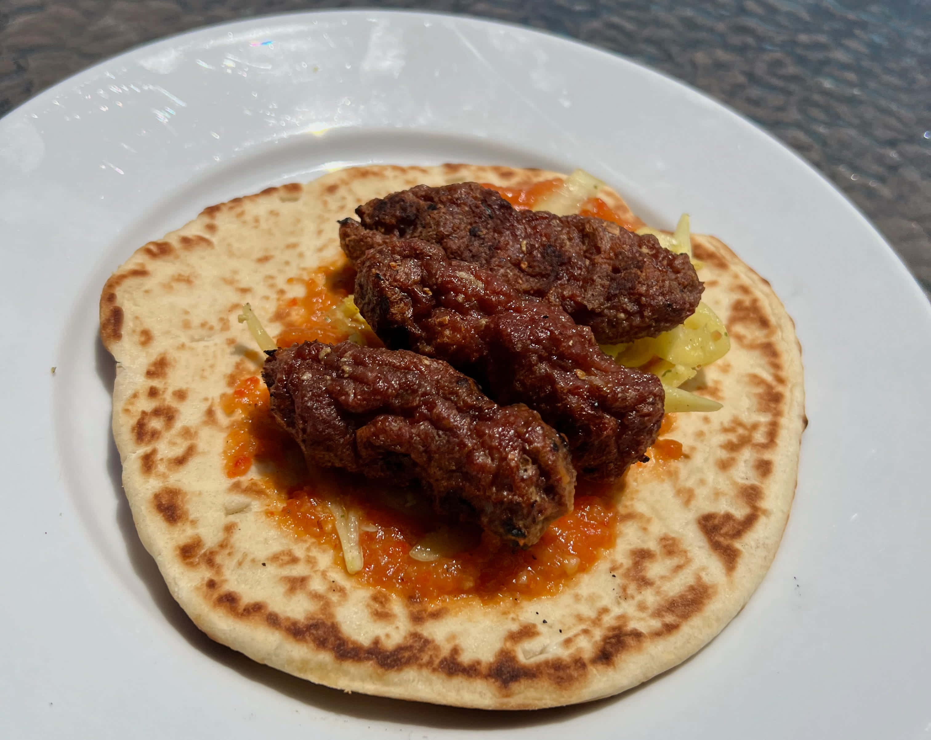 肉 桌布 壁紙 — 一個特寫鏡頭，顯示白色盤子上兩顆深色肉丸放在扁麵包上，搭配醬汁和高麗菜絲。