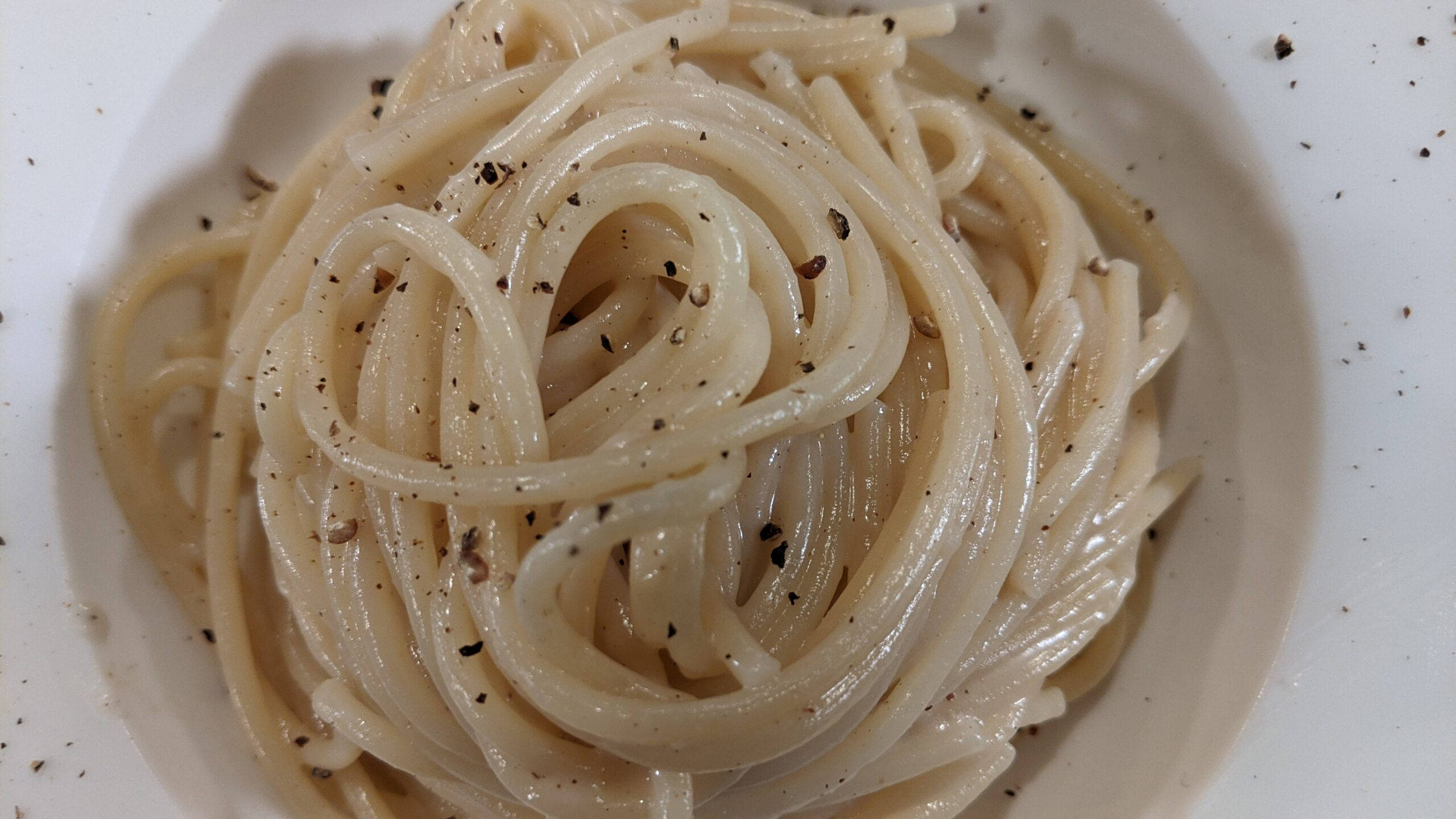 烹飪 桌布 壁紙 — 一個特寫鏡頭，顯示白色碗中纏繞的奶油義大利麵，上面撒上新鮮磨碎的黑胡椒。