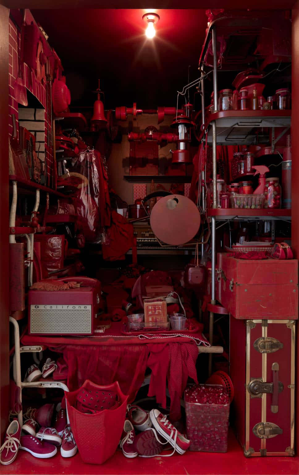 Red Room 桌布 壁紙 — 一個狹窄雜亂的房間，沐浴在強烈的紅光中，充滿了不匹配的紅色物品，從鞋子到行李箱和架子。