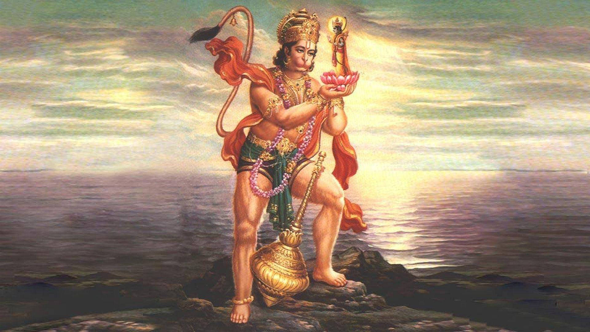 hanuman art 桌布 壁紙 — 一個猴頭神聖身影站在岩石海岸上，手持蓮花和狼牙棒，背景是閃耀的日落天空。