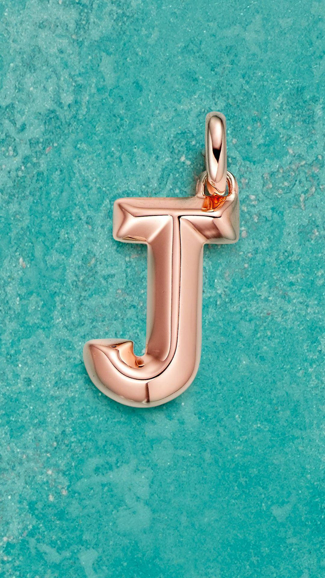 J 桌布 壁紙 — 一個玫瑰金字母J吊墜，帶有拋光曲線，放置在紋理綠松石表面上。