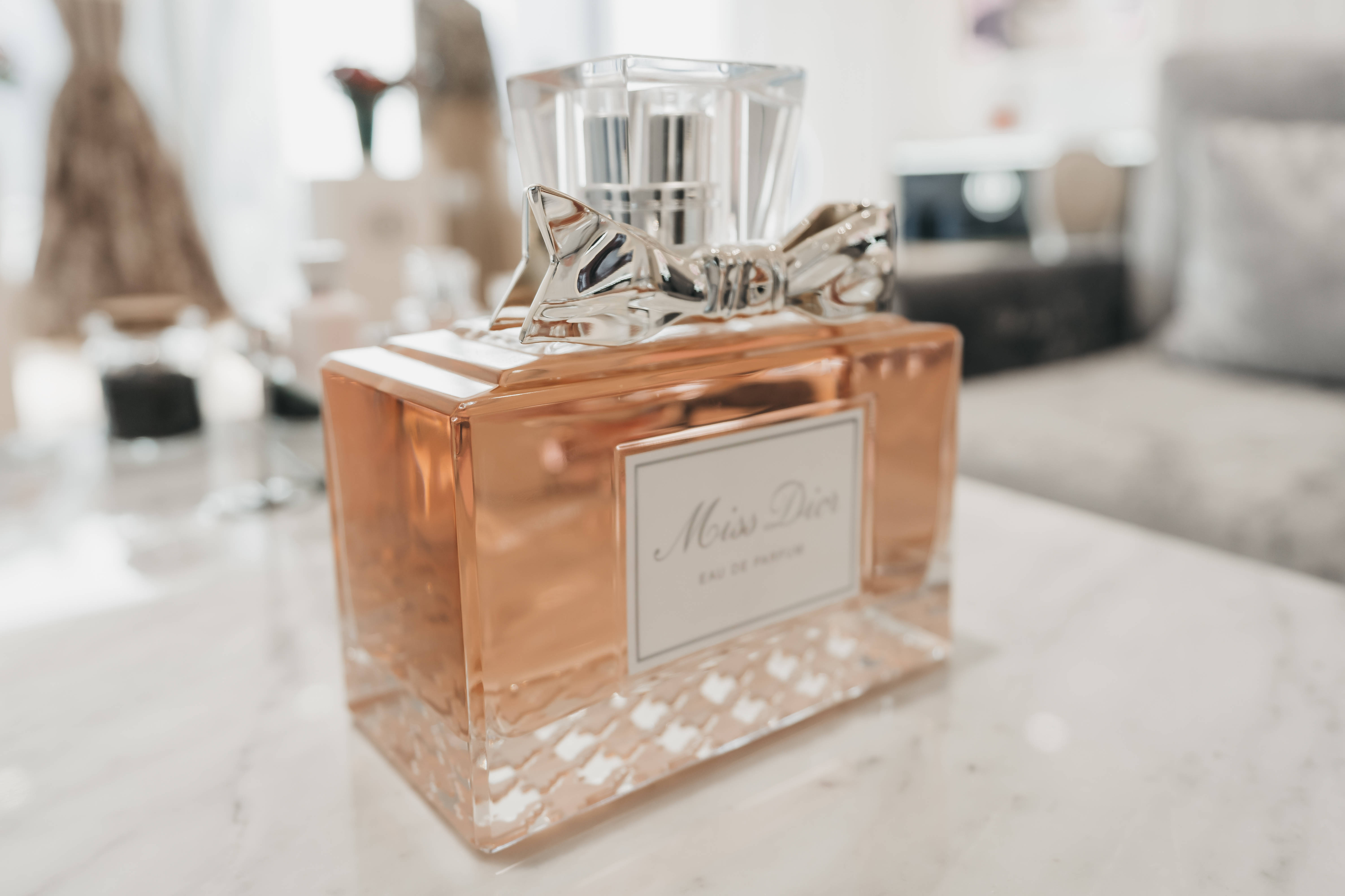 Christian Dior 桌布 壁紙 — 一個玫瑰金色 Miss Dior 香水瓶，配有銀色蝴蝶結，優雅地放在柔光房間的大理石表面上。