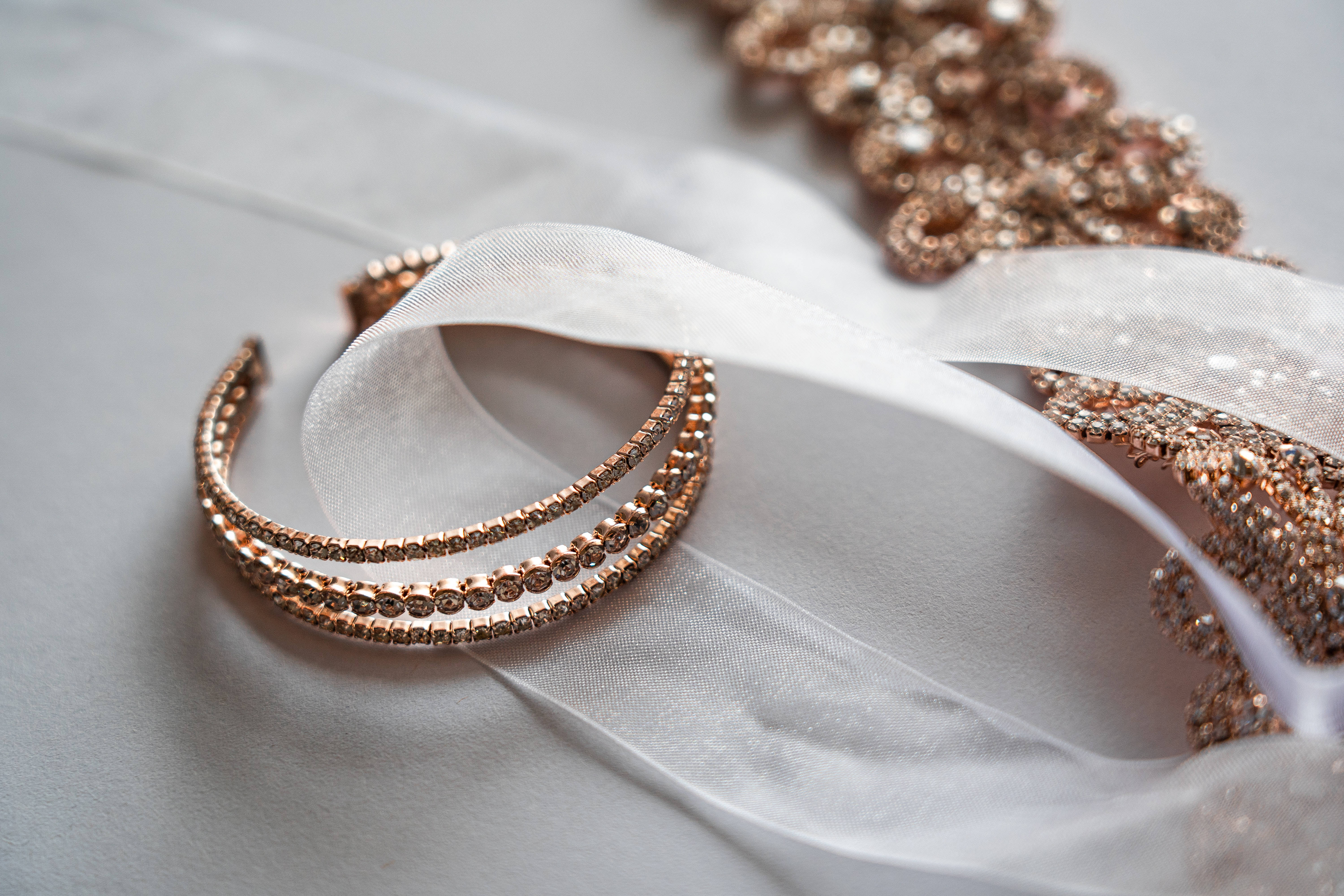 Gold Jewellery 桌布 壁紙 — 一個玫瑰金色鑲寶石頭帶和亮片布料優雅地放在柔軟的白色薄紗上，背景為中性色調。