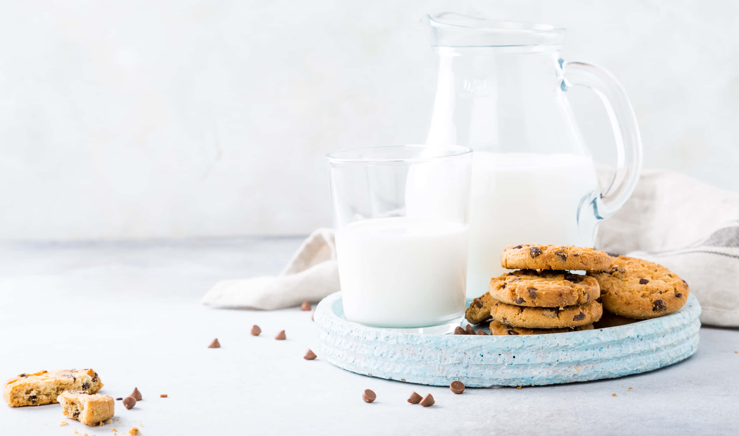 Cookies 桌布 壁紙 — 一個玻璃杯和一個牛奶壺放在一堆巧克力餅乾旁邊，放在一個有紋理的藍色盤子上，上面散落著碎屑。