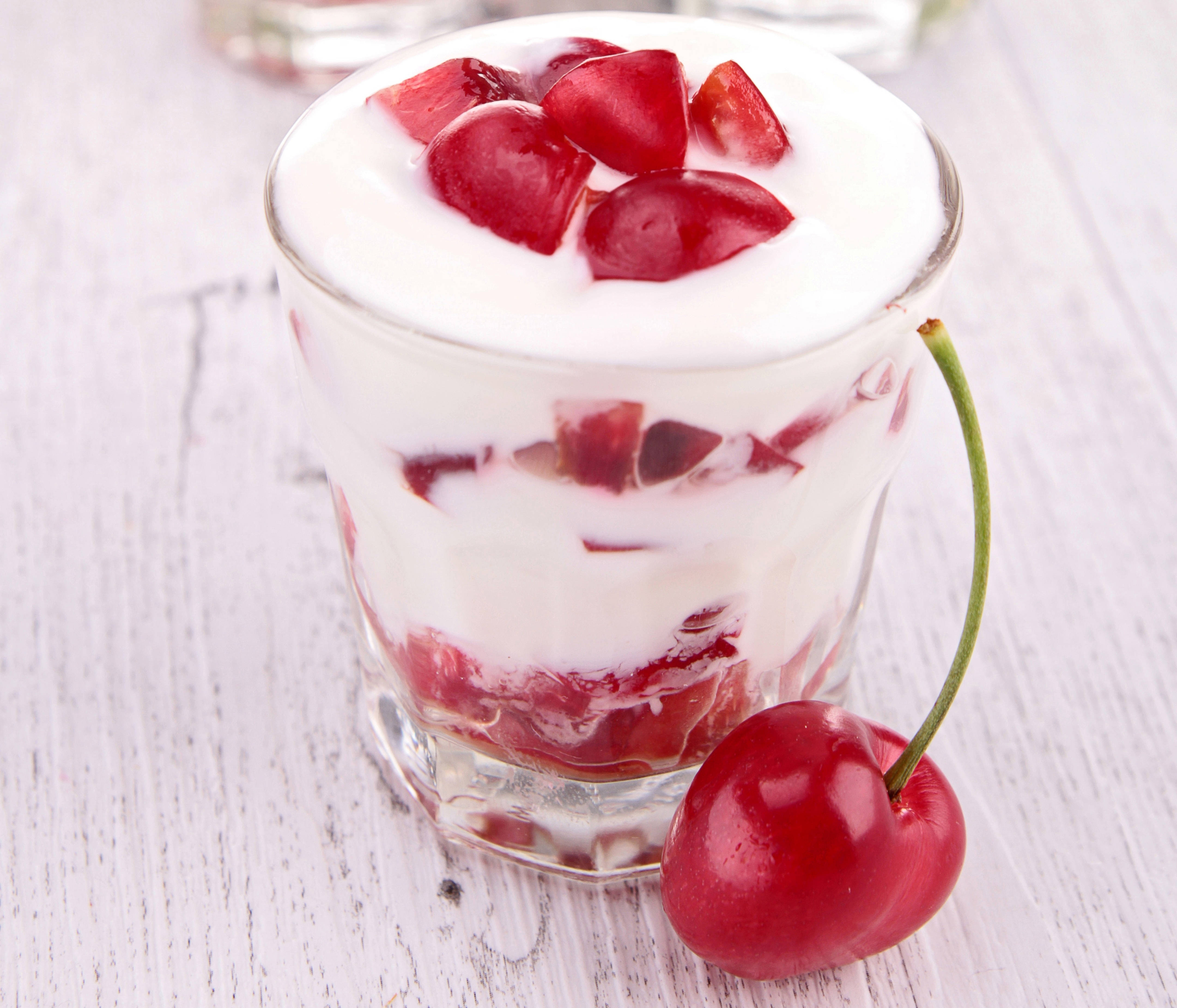 Cherry 桌布 壁紙 — 一個玻璃杯裝滿了奶油狀的優格和新鮮的紅櫻桃塊，放在白色木質表面上，旁邊還有一整顆櫻桃。
